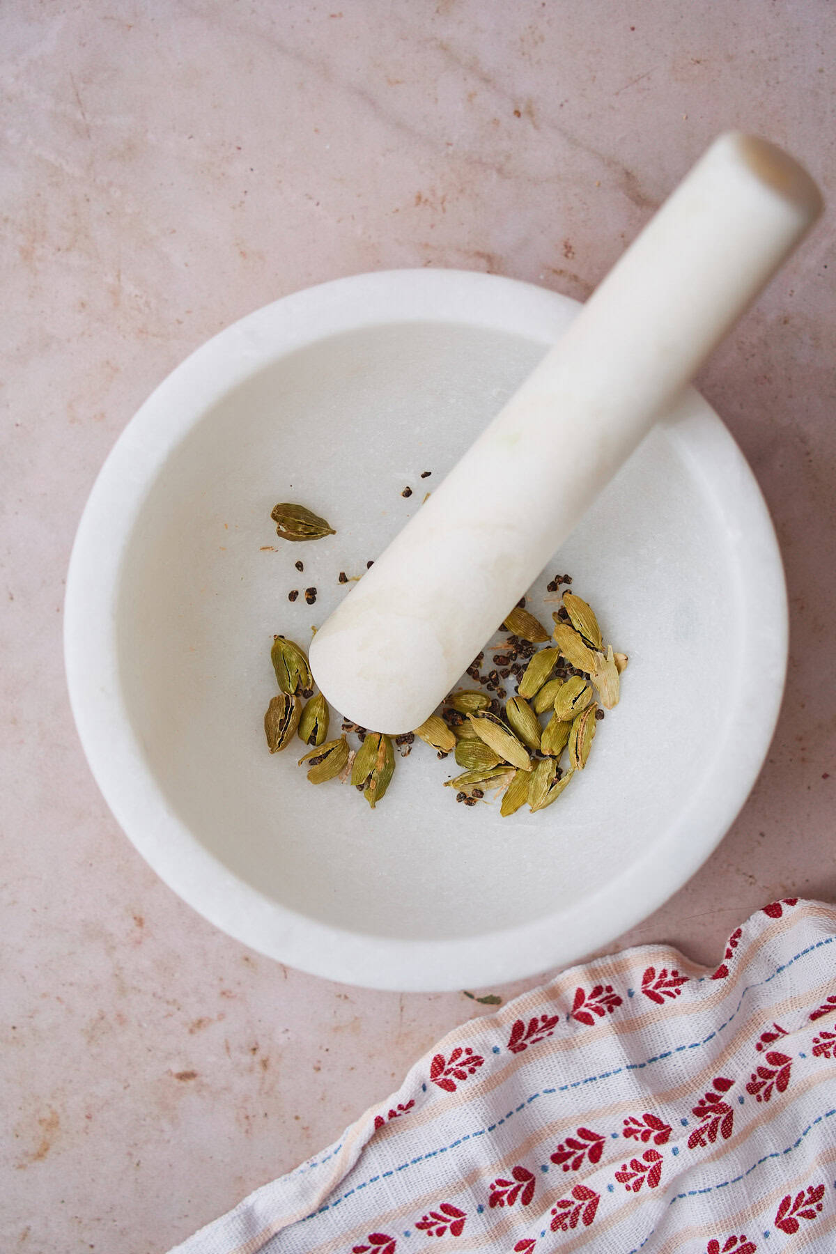 Green cardamom pods being crushed in a mortar and pestle.