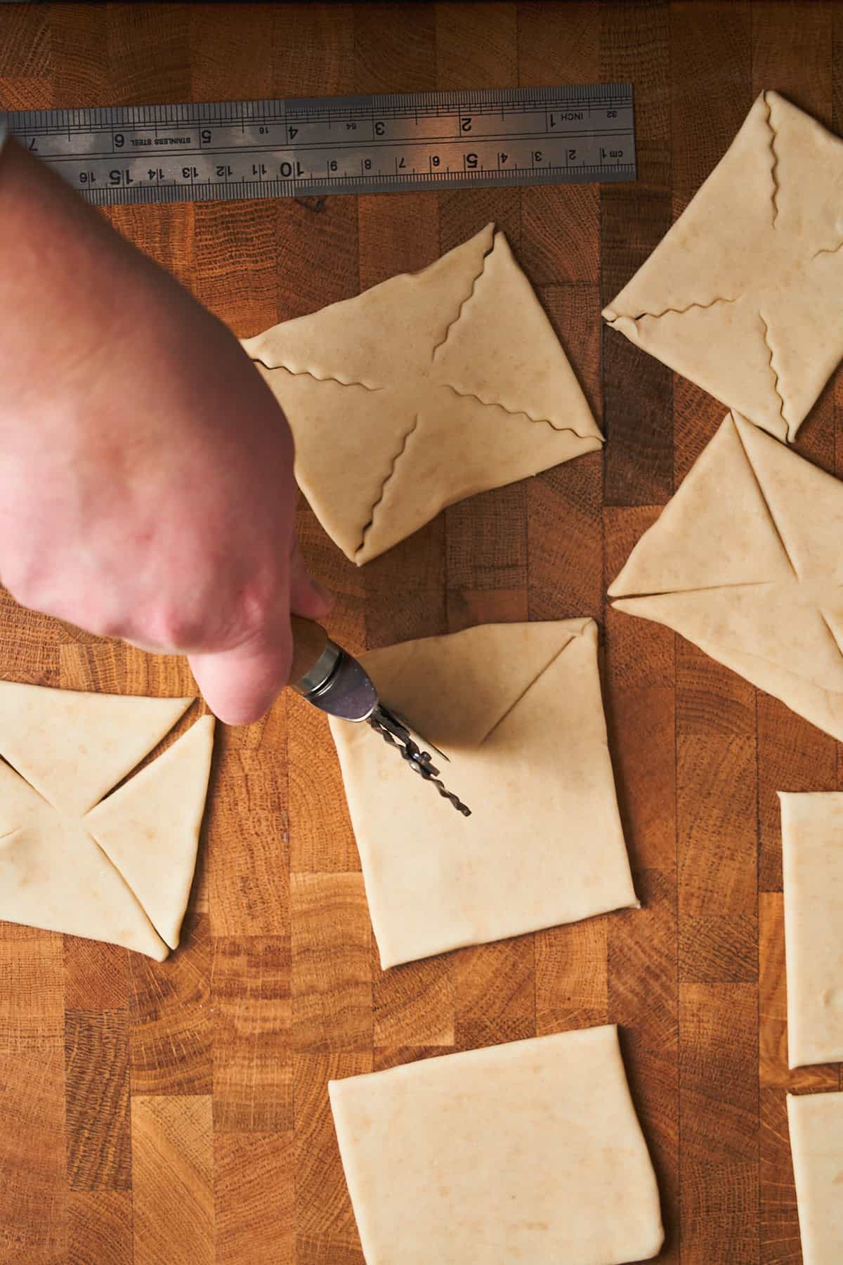 Squares cut of puff pastry, with a person cutting into the corners.
