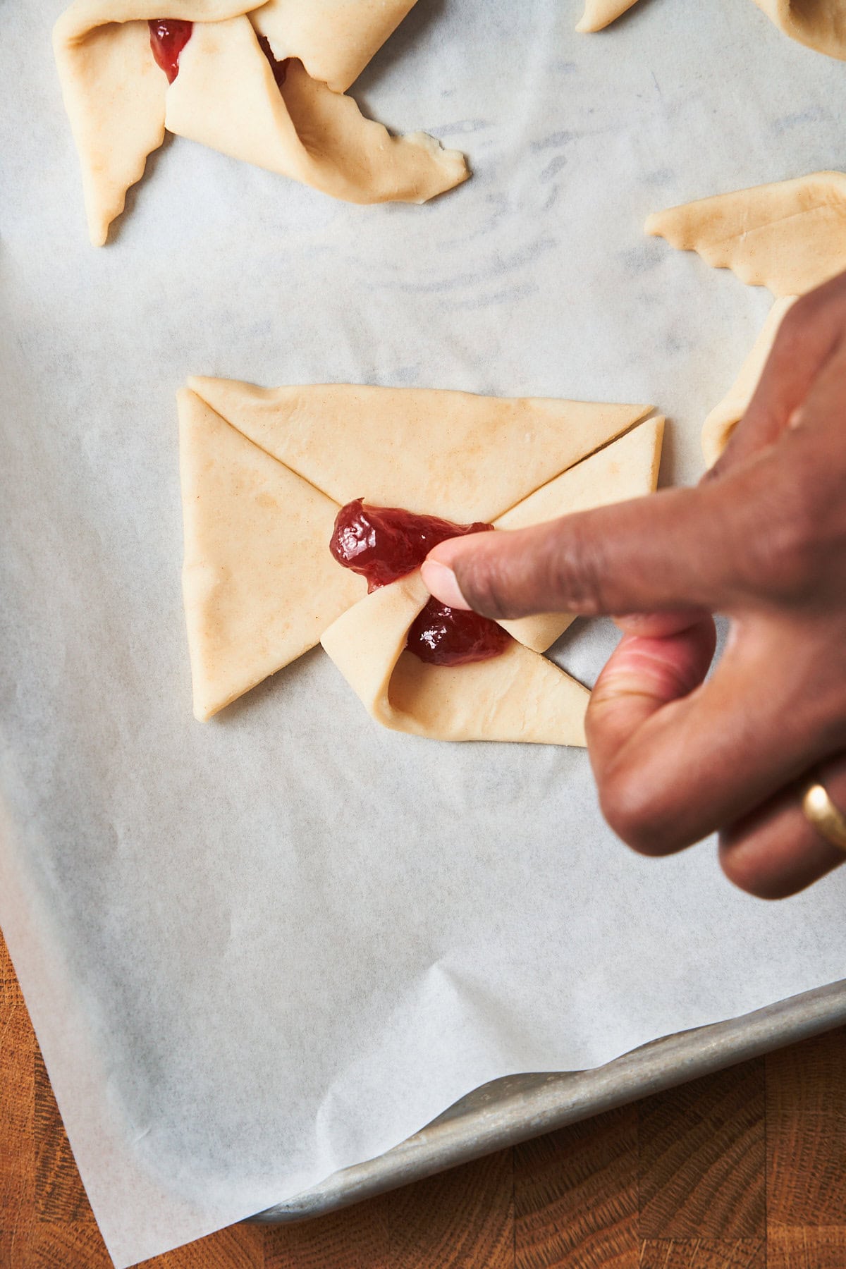 Hand pressing a second point of a cut puff pastry square over the center of jam to create a star shape.