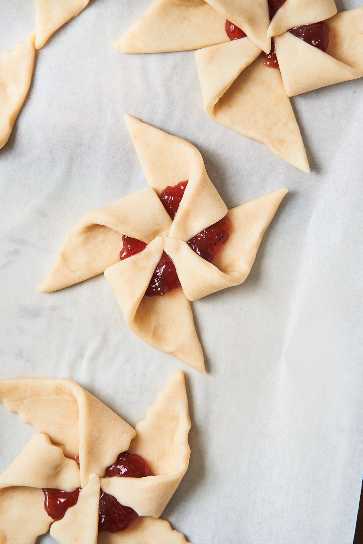 Pinwheel or star shaped uncooked puff pastry with jam fillings on a baking sheet with parchment.