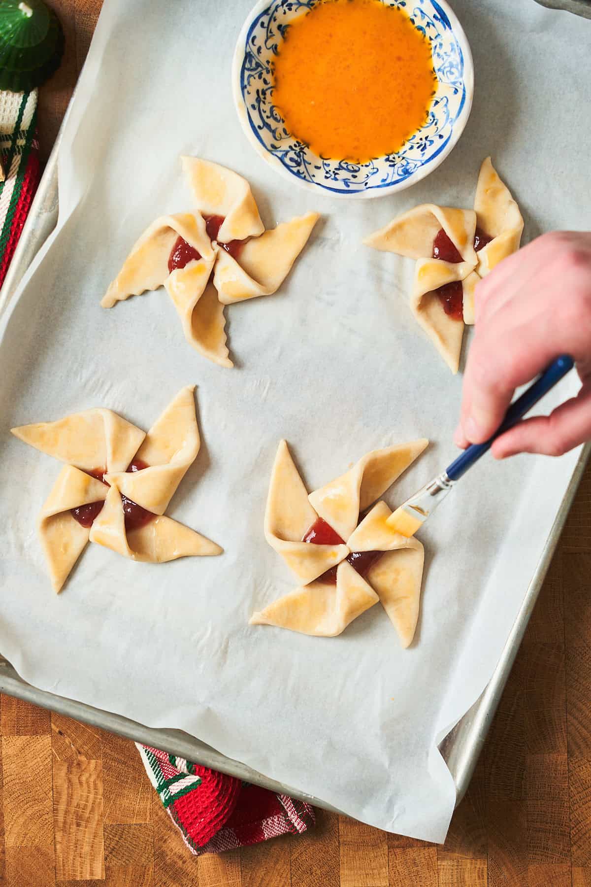 Hand brushing star shaped puff pastry tarts filled with jam with egg wash.