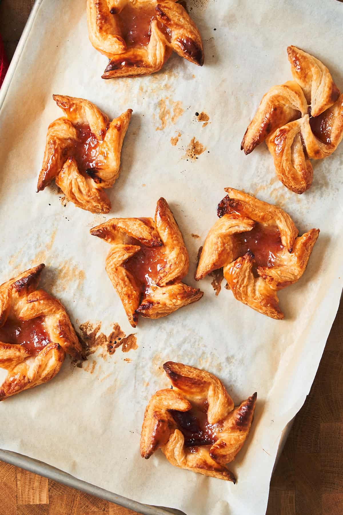 Puffed and golden puff pastry pinwheels with a jam filling on a parchment paper lined baking sheet.