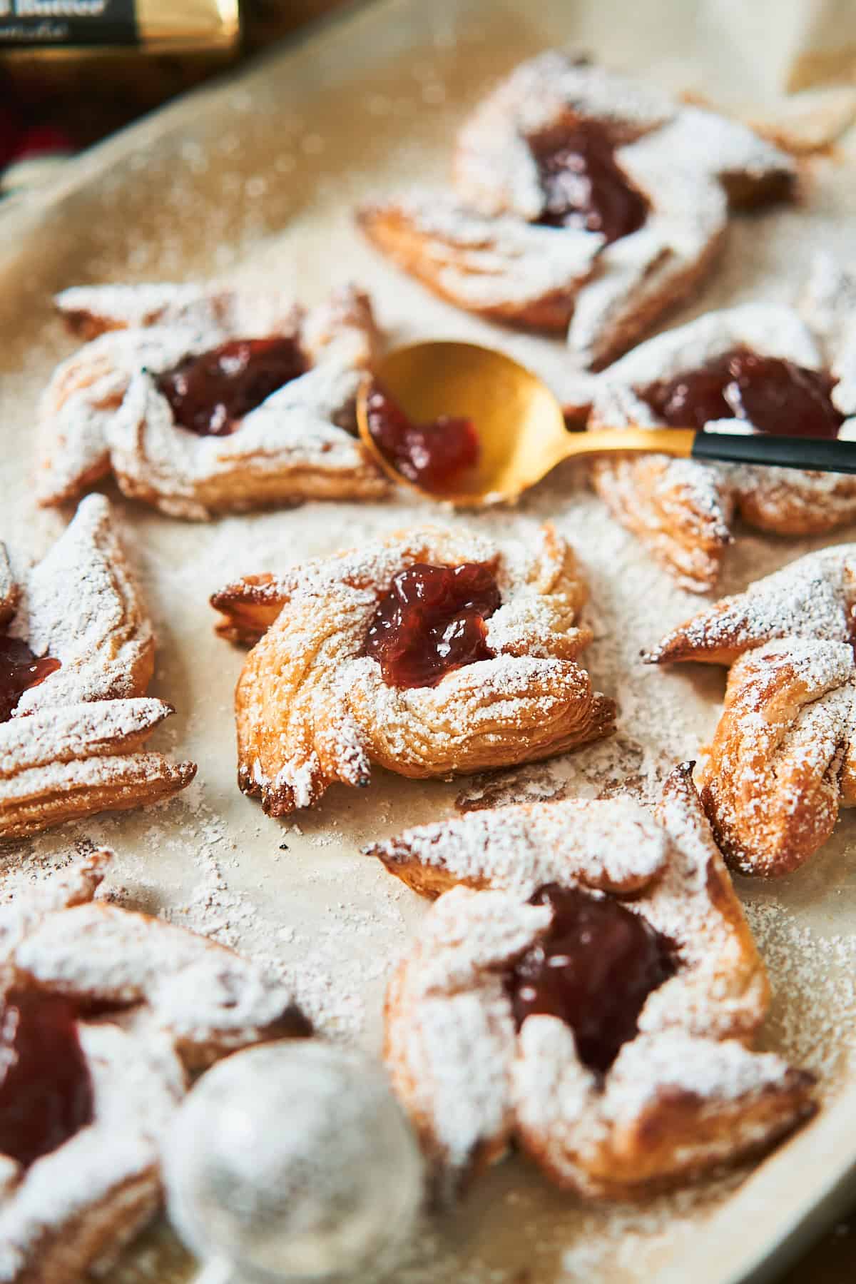 Puff pastries filled with jam and topped with powdered sugar on a baking sheet with parchment paper.
