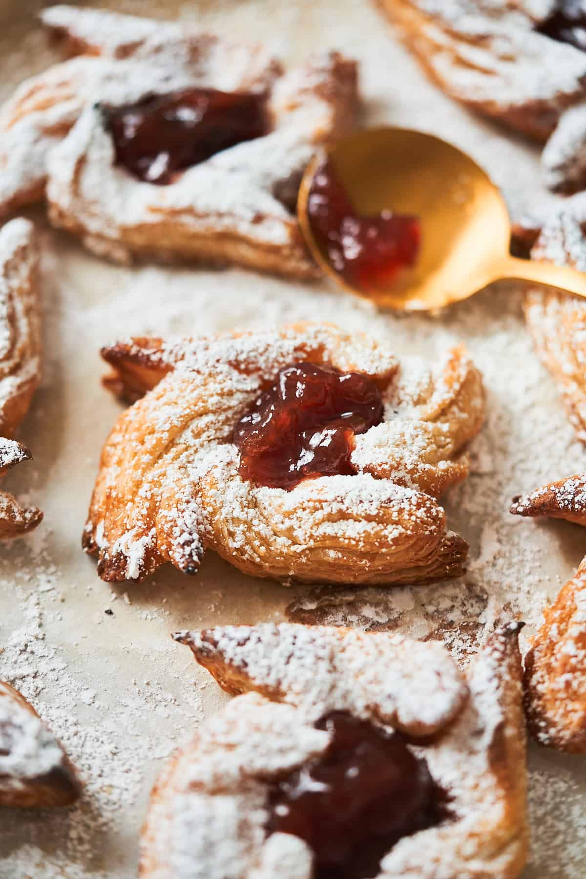 Stunning Finnish star cookie made with puff pastry on a baking sheet, being filled with jam after being dusted with powdered sugar.