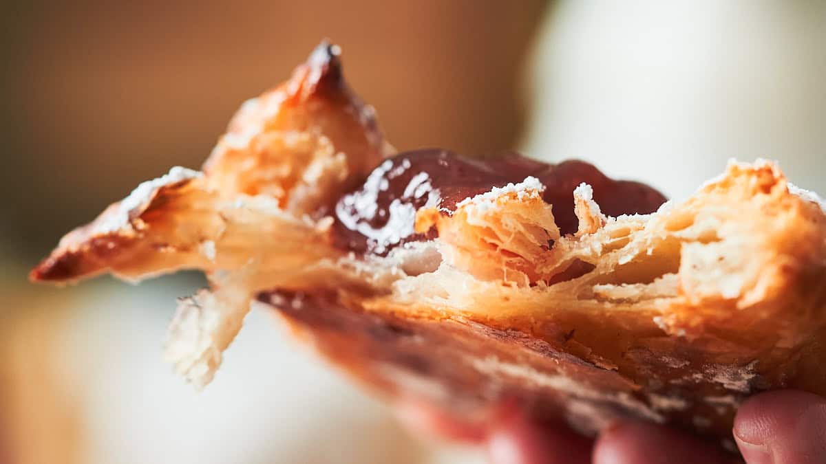 Very close up shot showing very flaky layers on a pastry filled with jam.