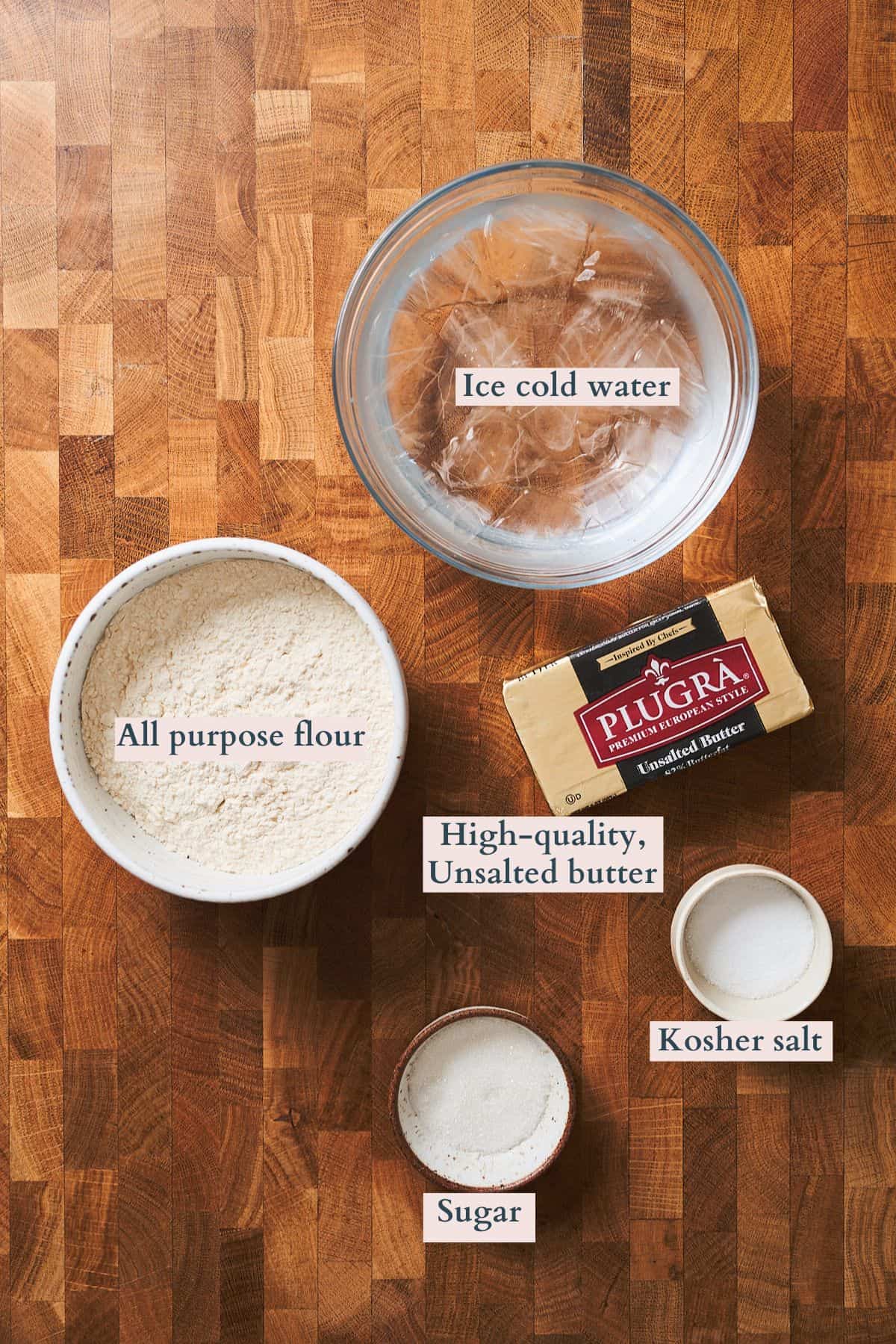 Ingredients for baking: flour, butter, salt, and sugar on a wooden surface.