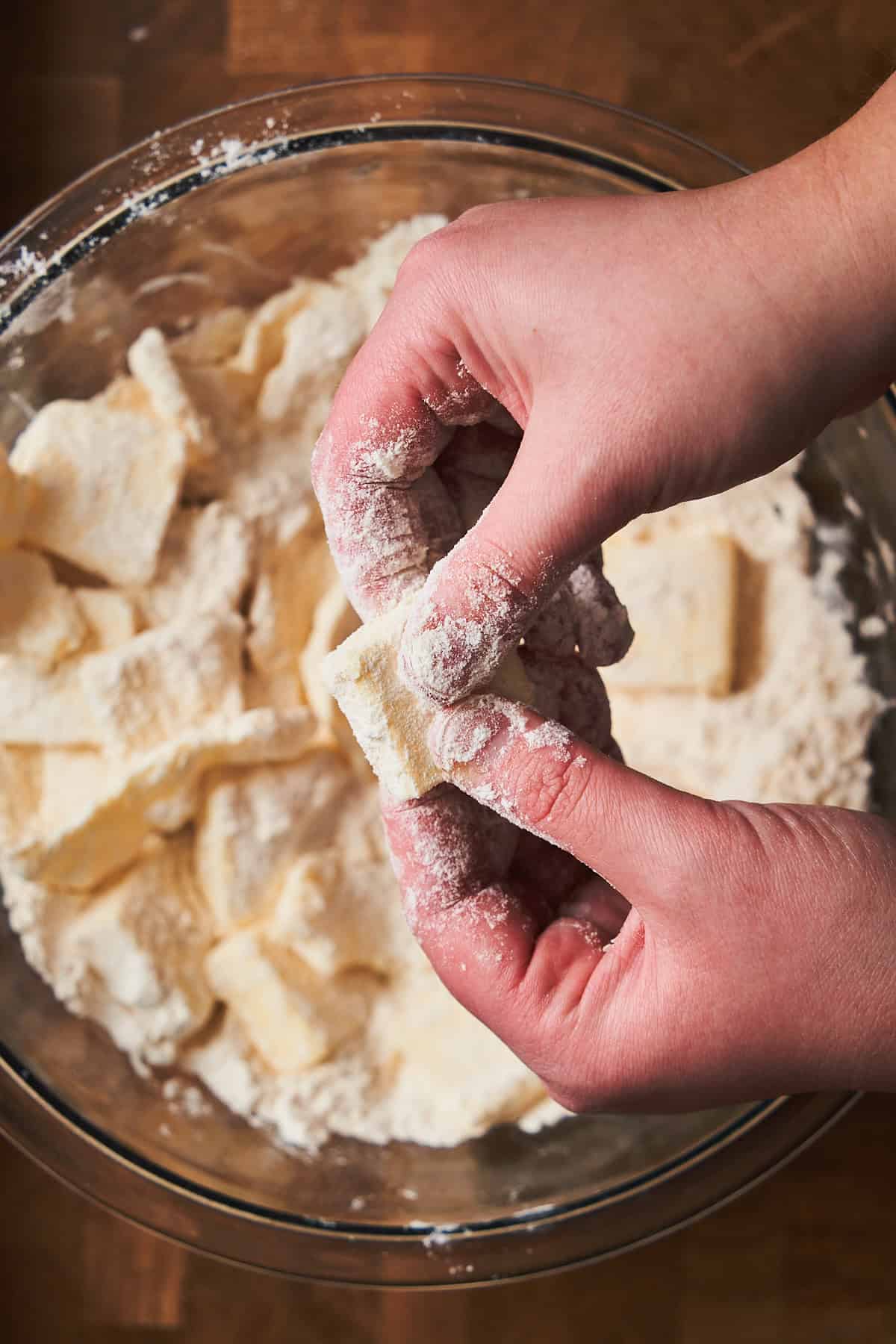 Two hands holding a chunk of butter coated in flour, pressing gently.