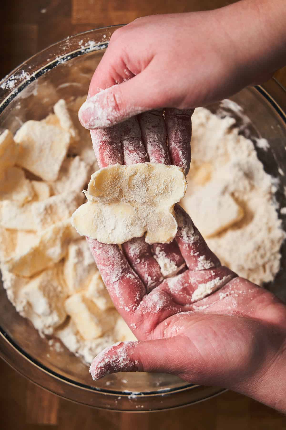 Hands holding a piece of flattened butter coated in flour.