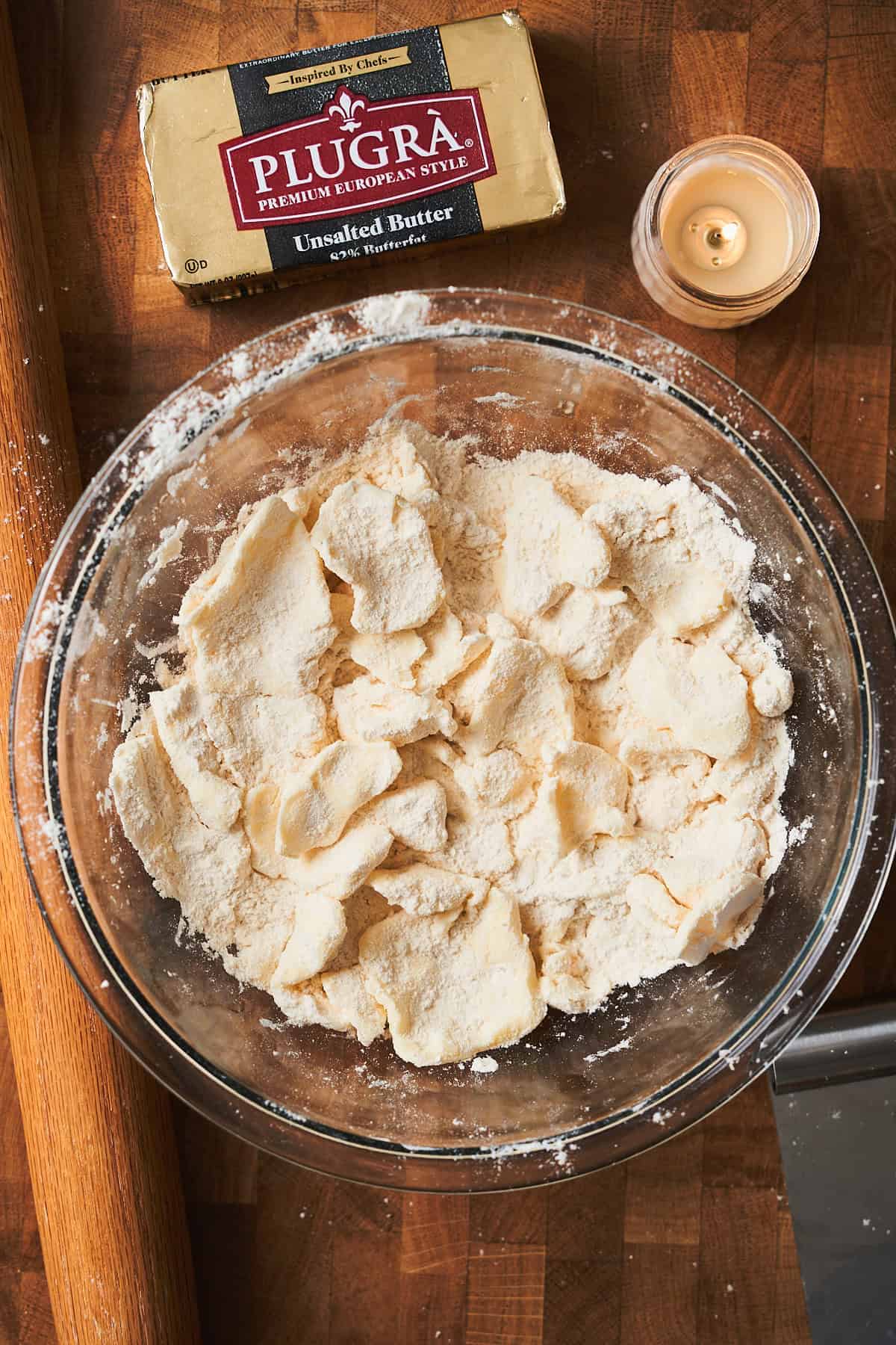 Bowl of flattened butter sheets coated in flour in a bowl with a candle nearby.