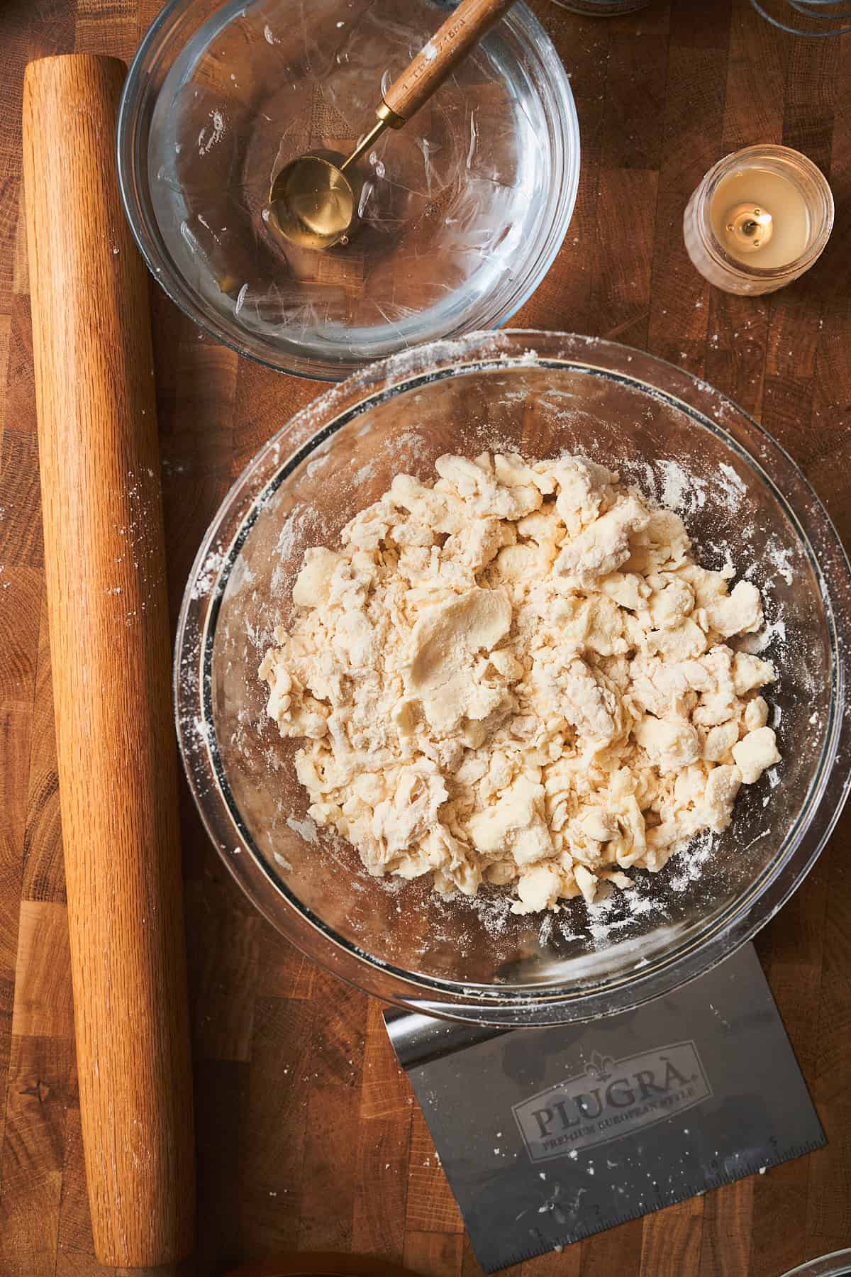 Bowl of puff pastry dough beginning to form with a bowl of water and a small candle nearby.