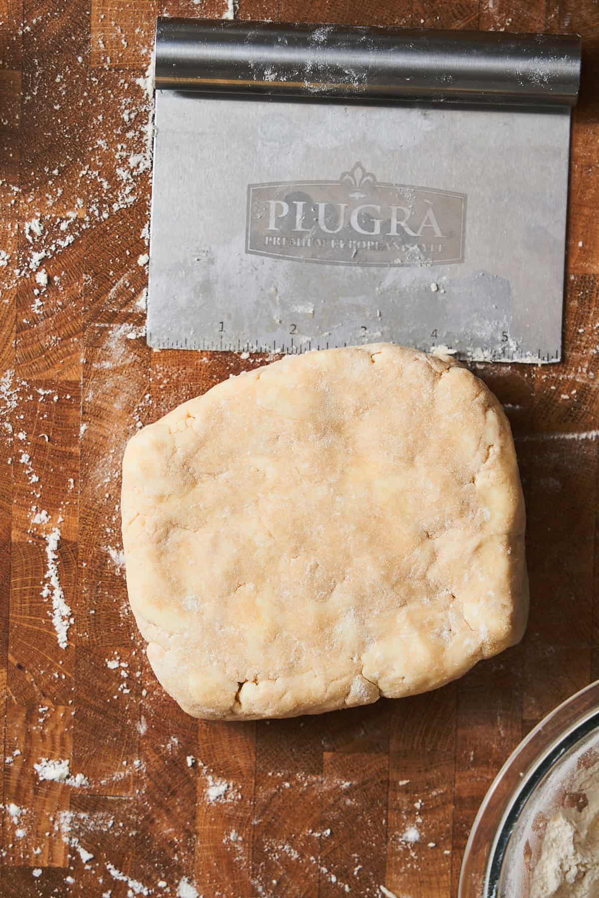 Square of dough on a lightly floured surface with a metal bench scraper near by.
