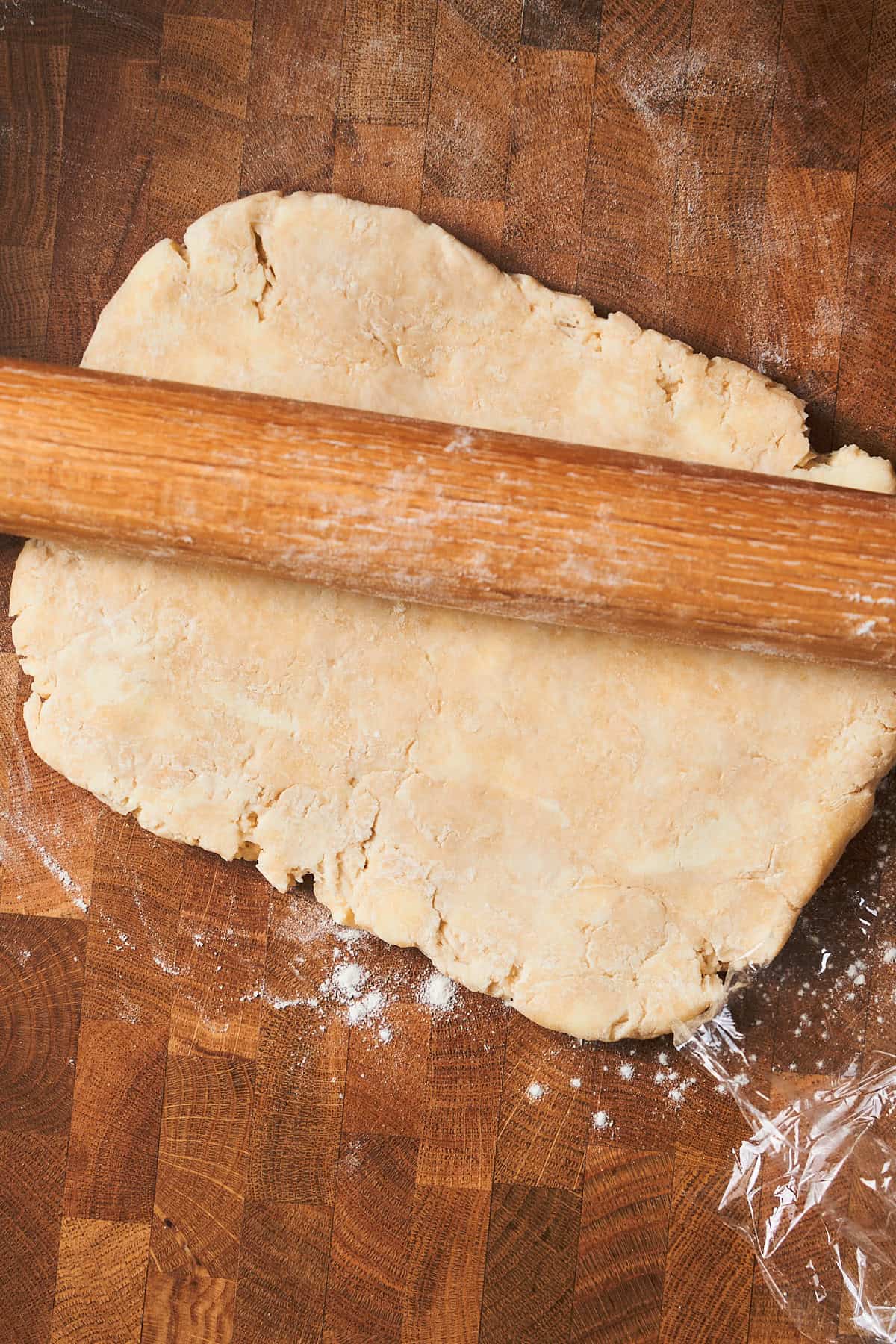 Rough puff pastry dough forming and being rolled out on a floured wooden surface.