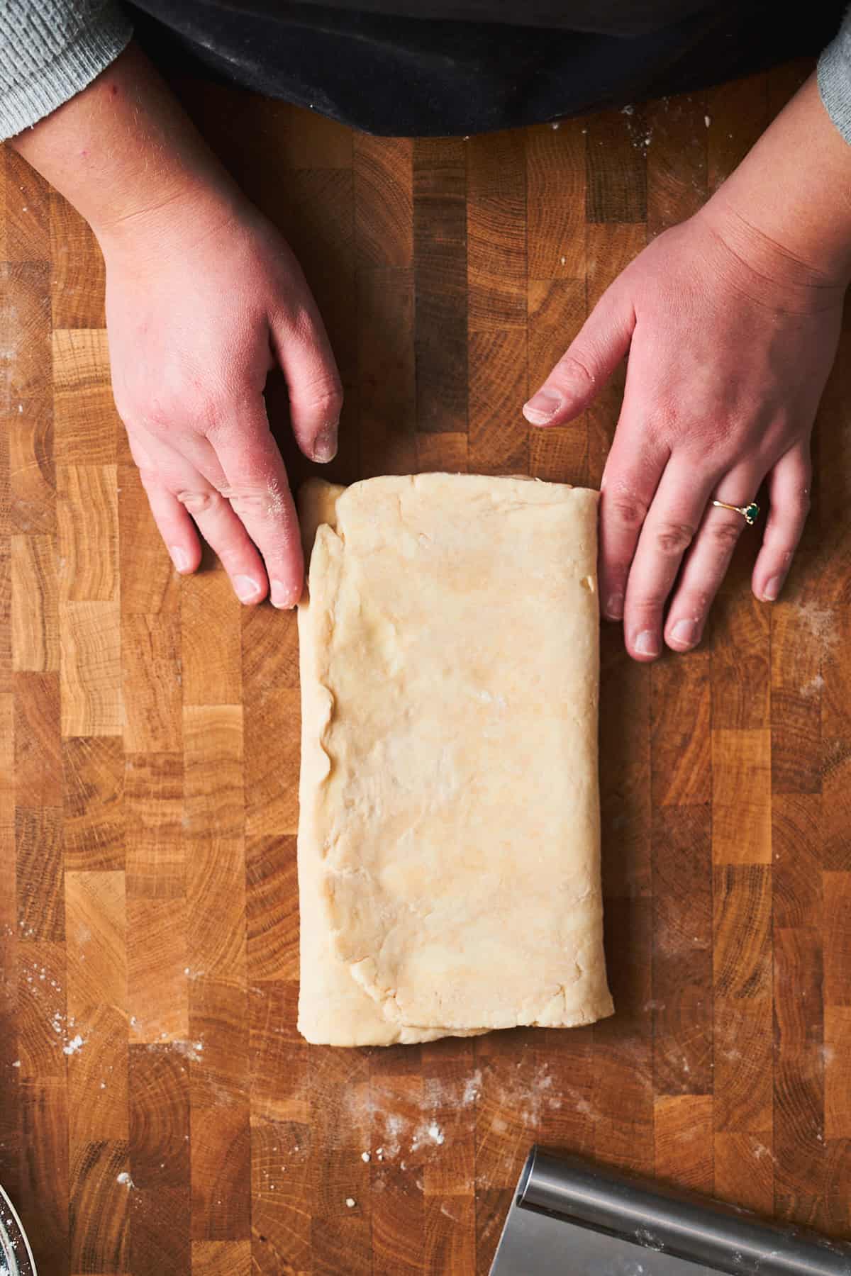 Hands holding freshly folded puff pastry dough.