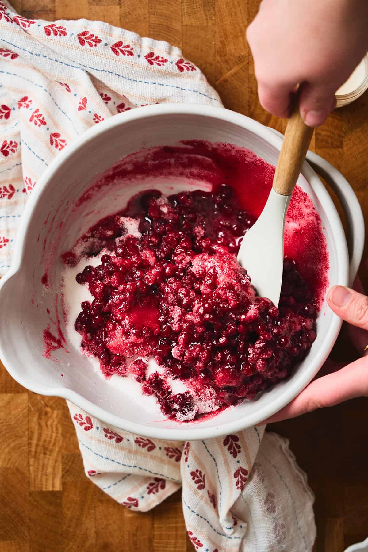 Hand stirring lingonberries with a rubber spatula.