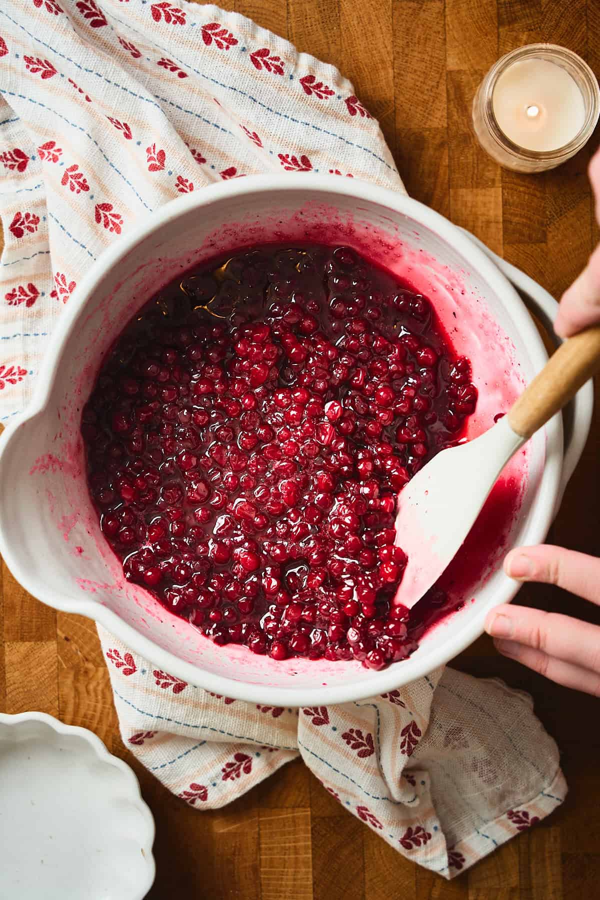 Hand stirring lingonberries in a bowl with a rubber spatula and macerating them.