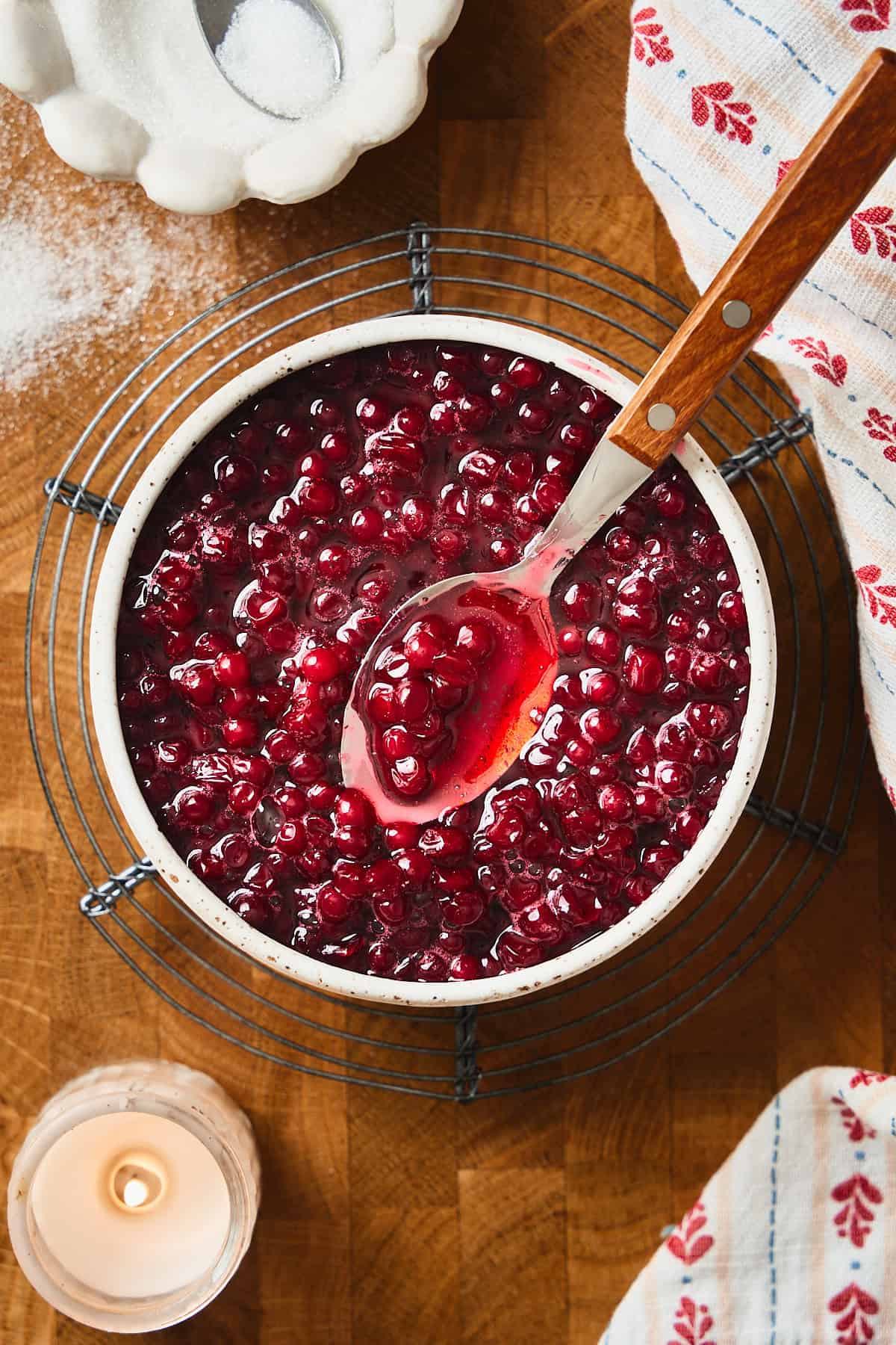 Overhead view of beautiful bright red lingonberries with a spoon in a ceramic container on a wood background.