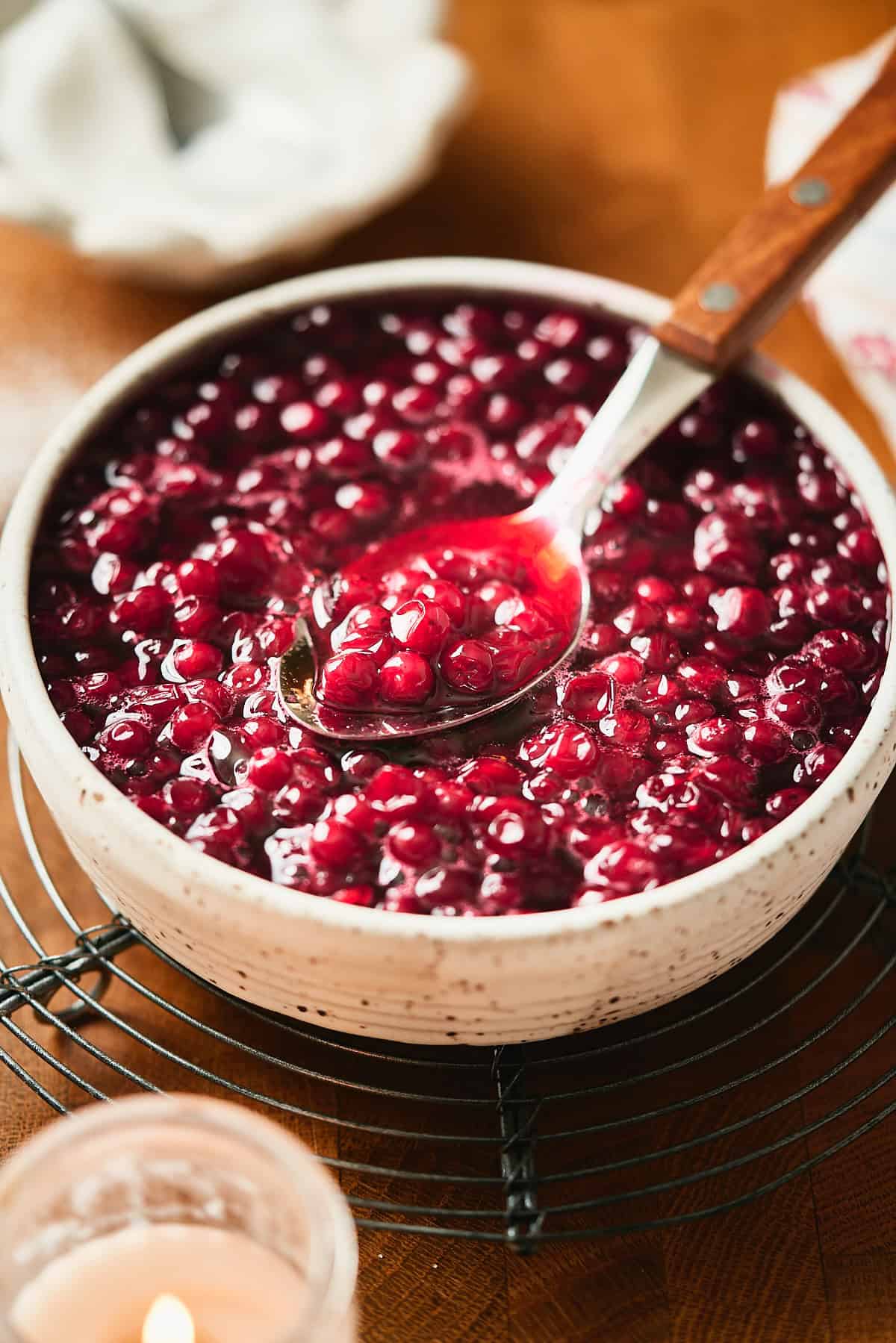 Lingonberries in a thick bright red syrup with a candle nearby on a wooden background.