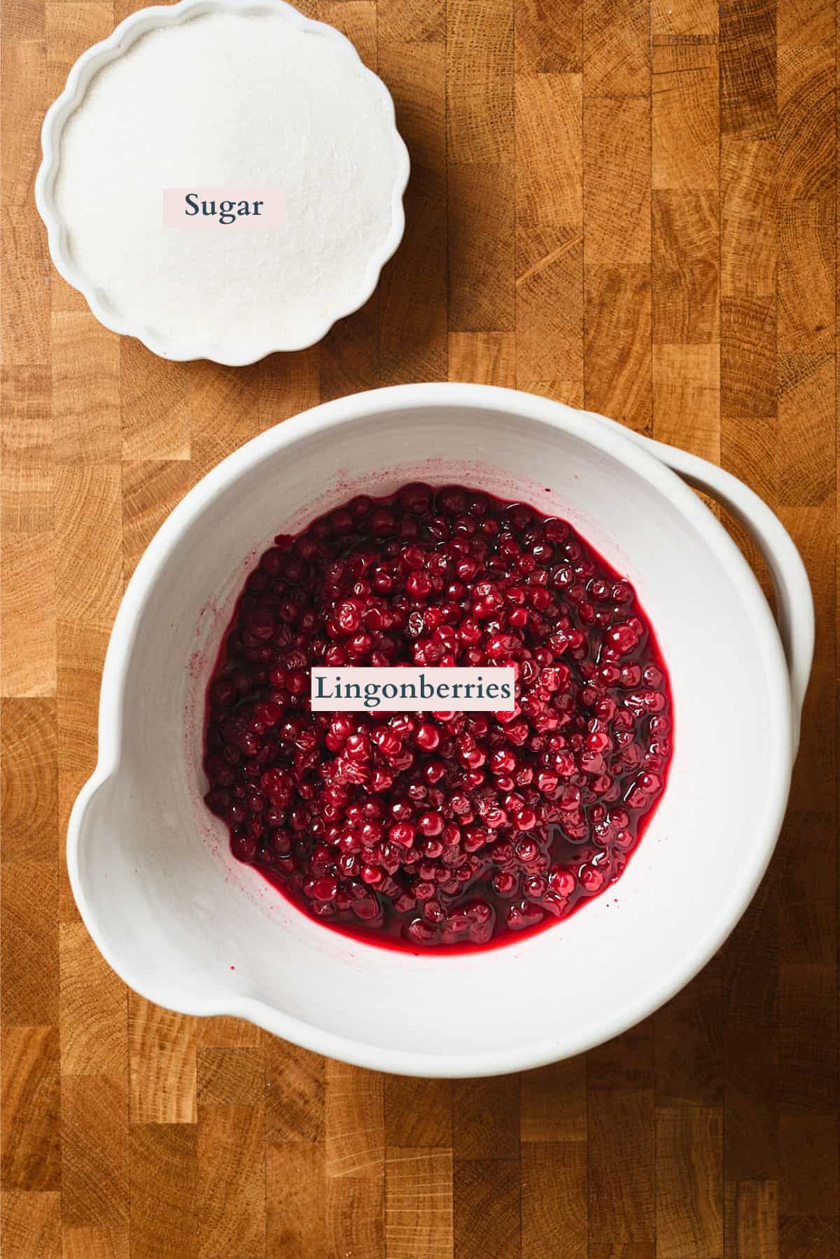 Lingonberries and sugar laid out on a wooden table and labeled.