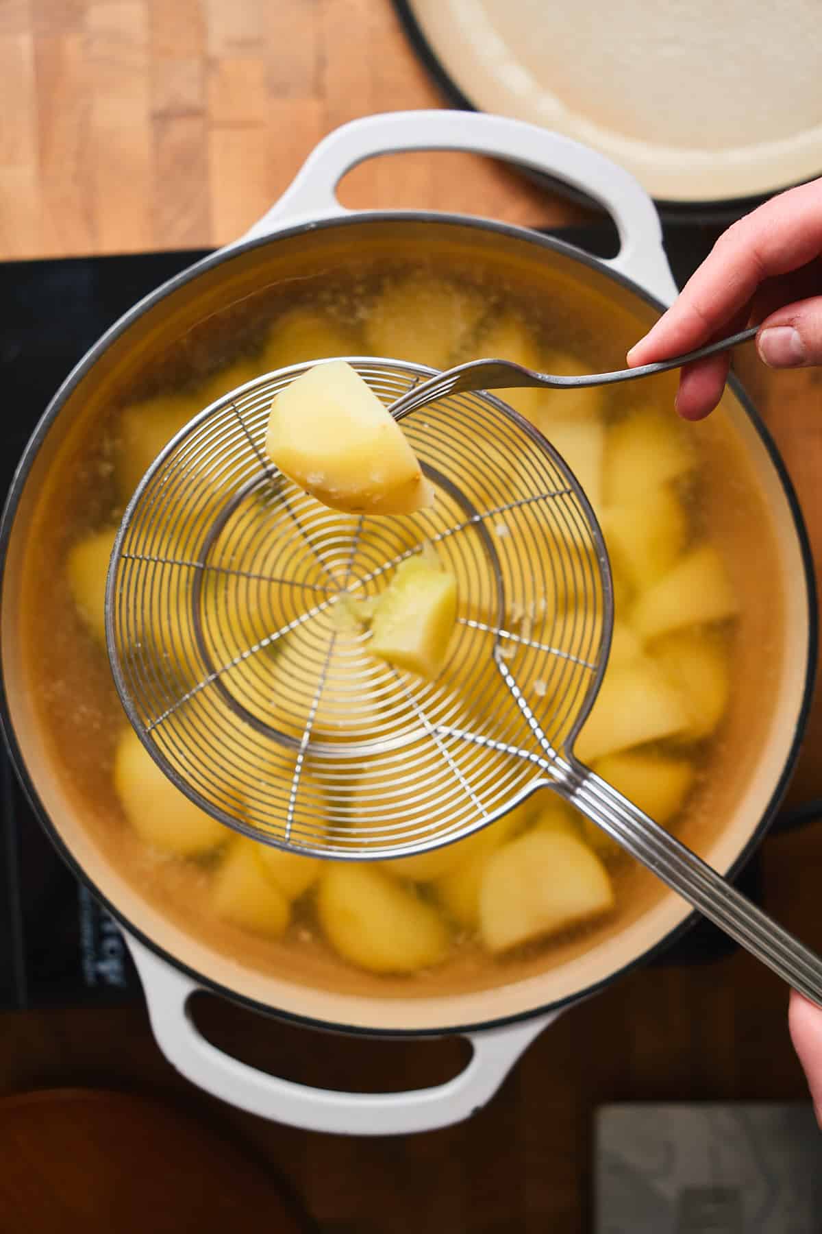 Hand showing a fork poked into a cooked potato to show they are ready to be mashed.