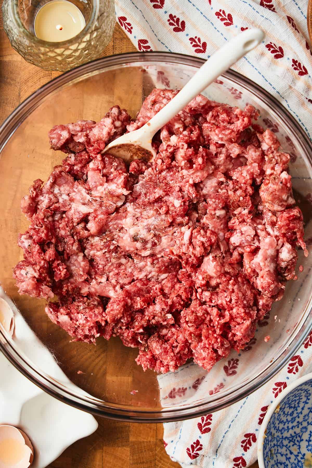 Mixing together beef, pork, spices, and salt in a bowl to make meatballs.