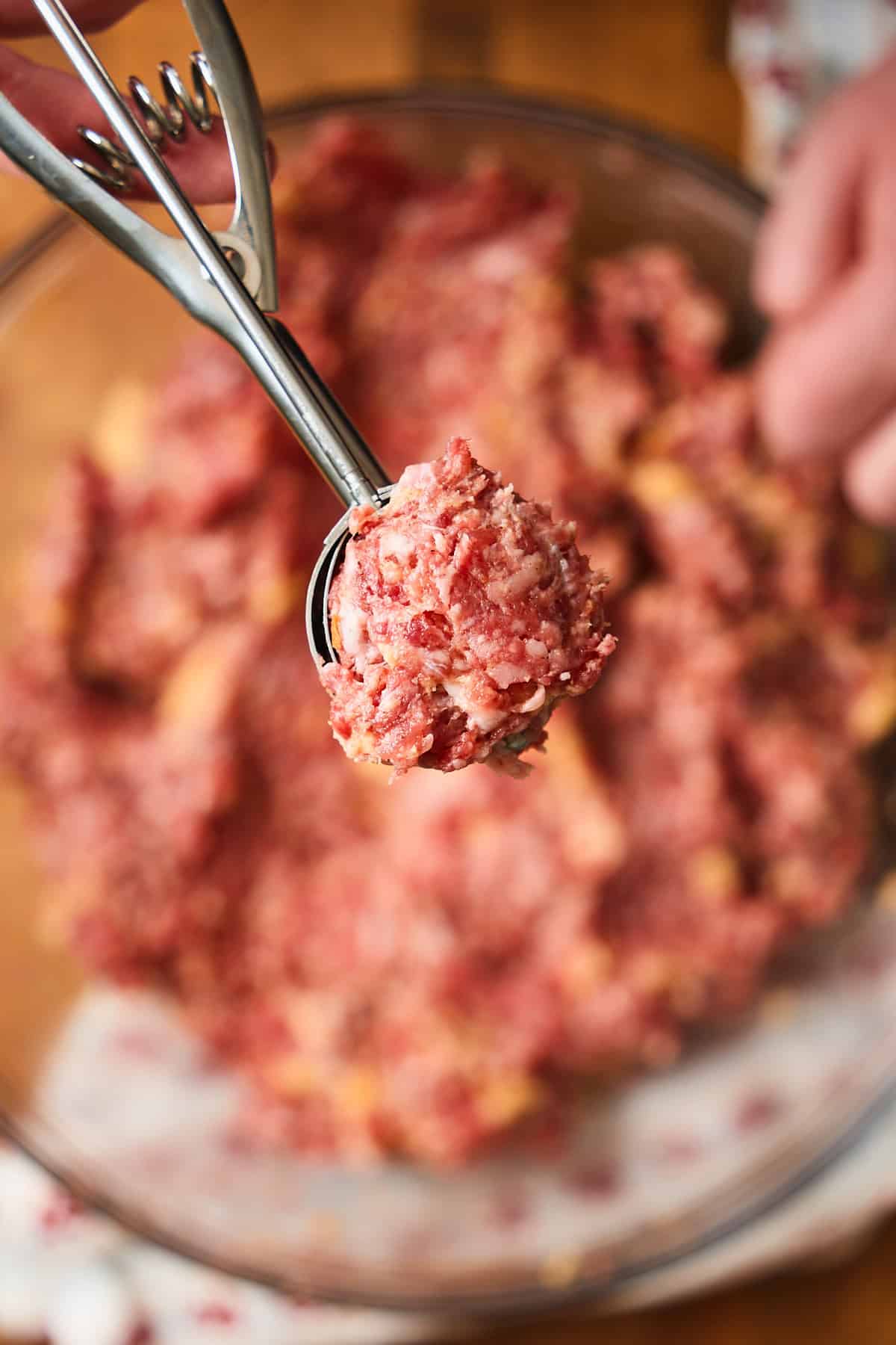 Small cookie scoop being held up to the camera with raw meatball mixture inside.