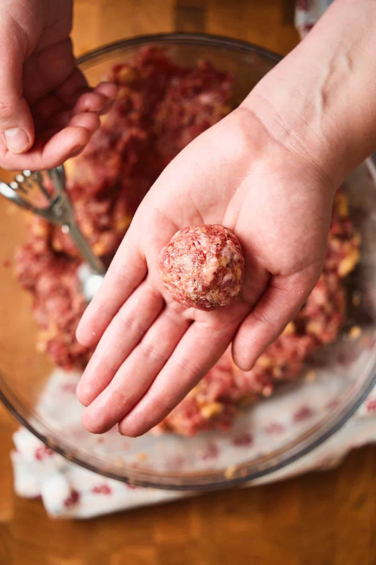 Hand holding a perfectly rolled raw Swedish meatball to the camera.
