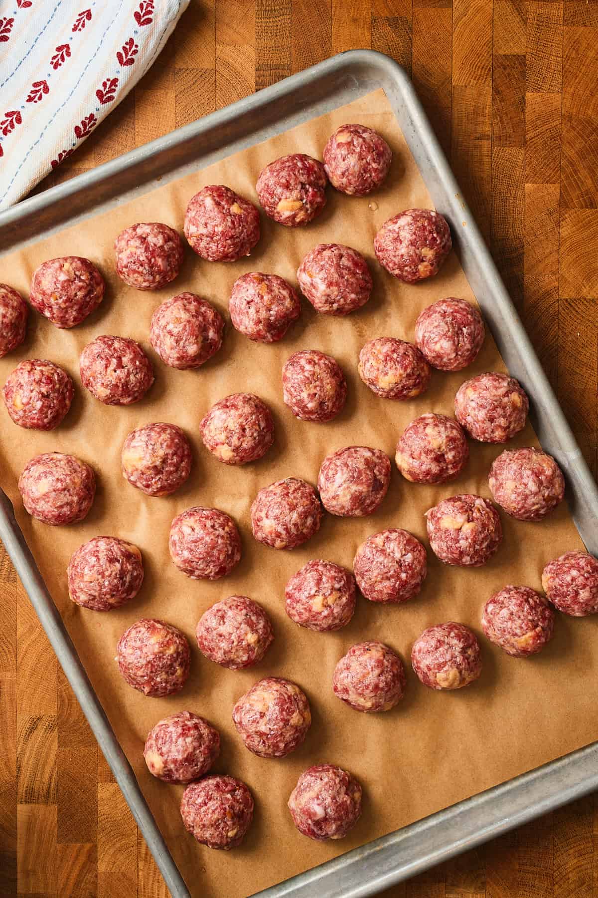 Rolled raw meatballs on a parchment lined baking sheet.