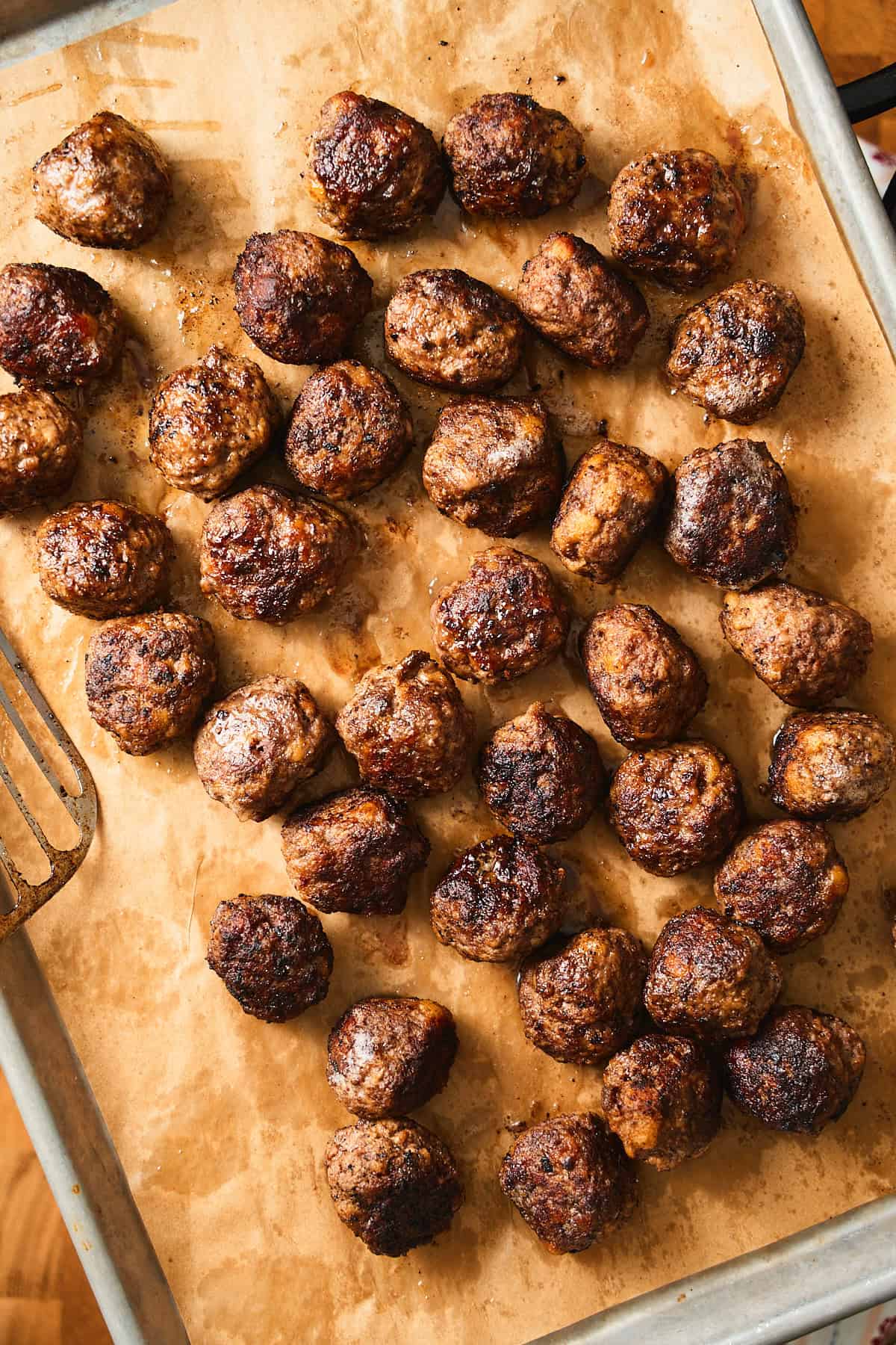 Cooked Swedish meatballs on a parchment lined baking sheet.