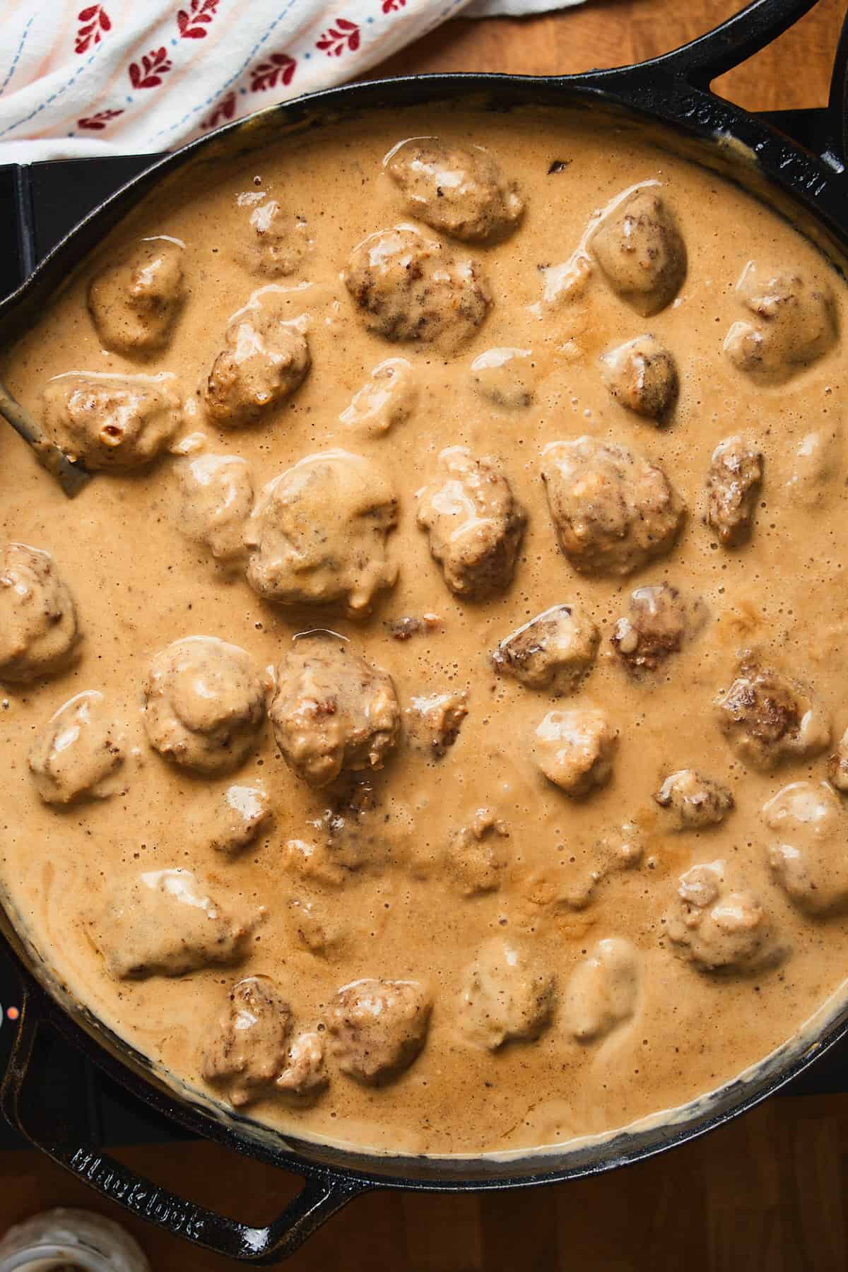Swedish meatballs simmering in a creamy gravy in a skillet.