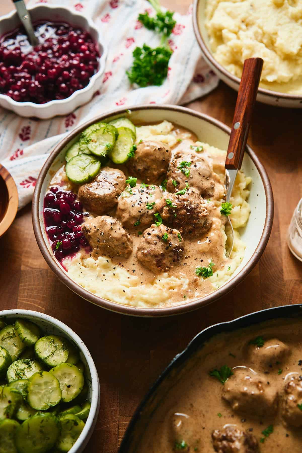 Bowl of Swedish meatballs on mashed potatoes with lingonberries, pickled cucumbers.