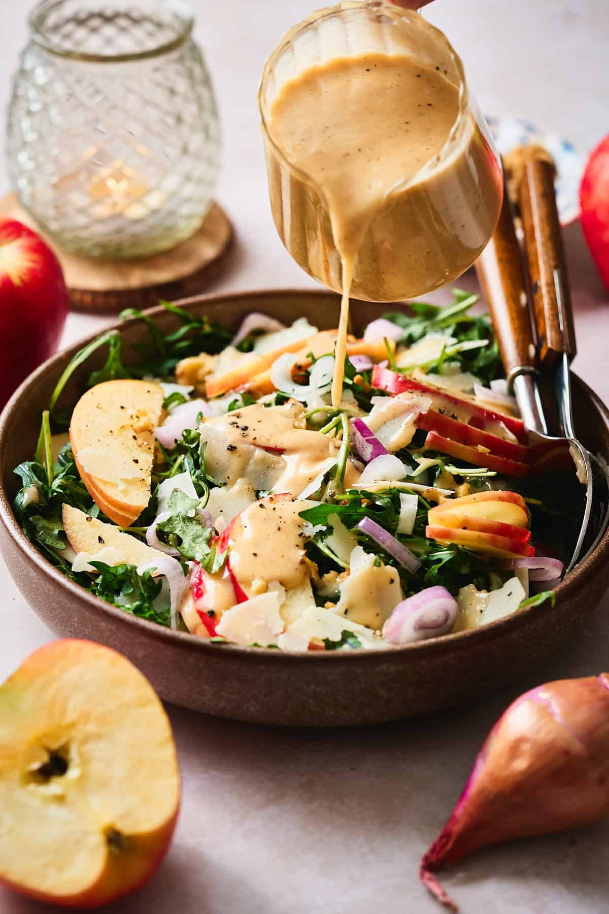 Pouring apple cider vinaigrette being poured onto an apple arugula salad.