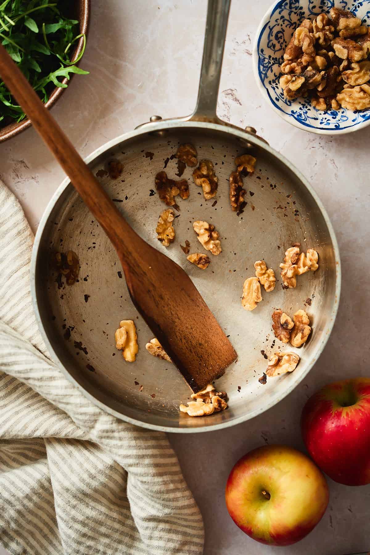 Toasting walnuts in a saucepan with apples, linens, and shallots nearby.