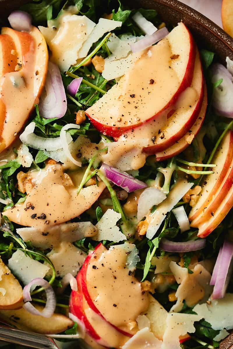 Gorgeous macro shot of an apple arugula salad topped with pecorino romano cheese, shallots, cider dressing, and fresh cracked pepper.