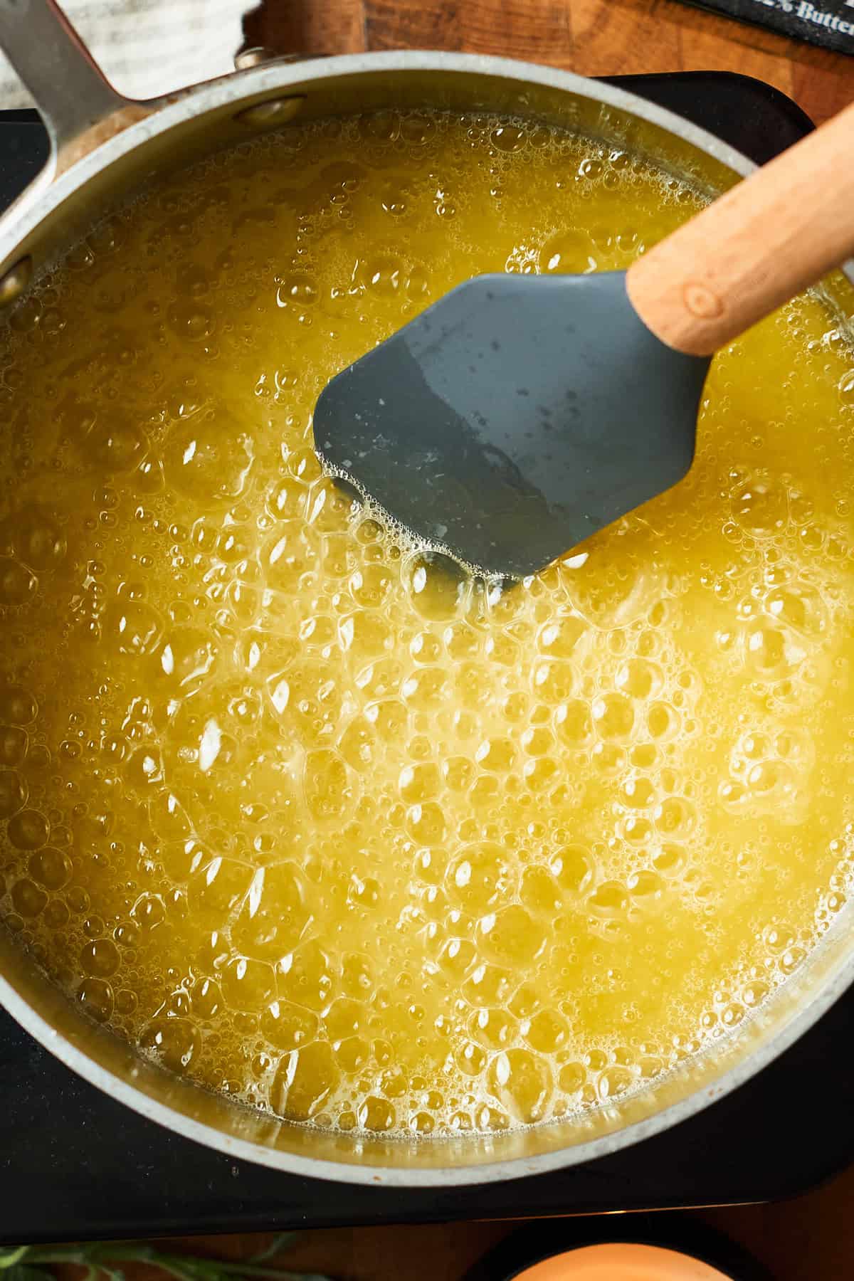 Foaming golden butter in a metal saucepan with a rubber spatula stirring it.