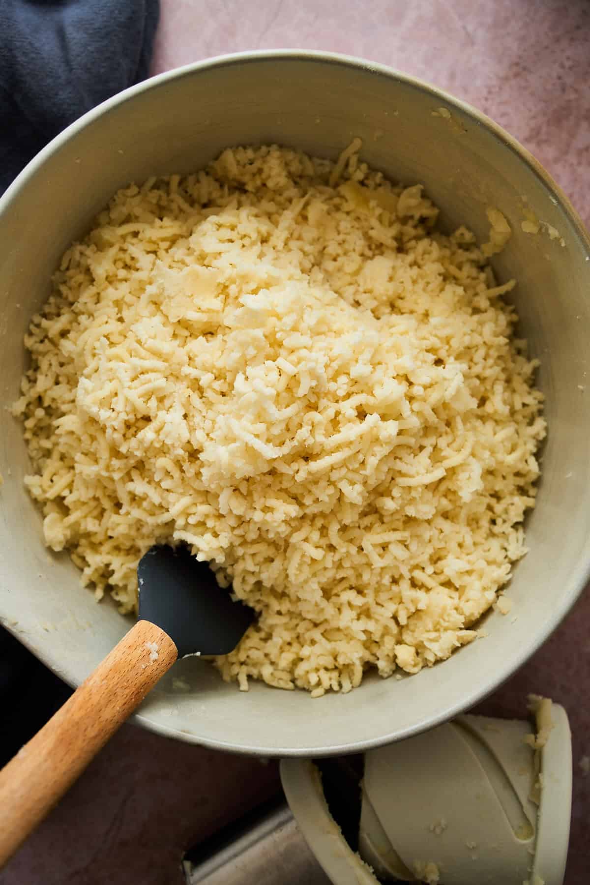 Riced potatoes in a large bowl with a rubber spatula.