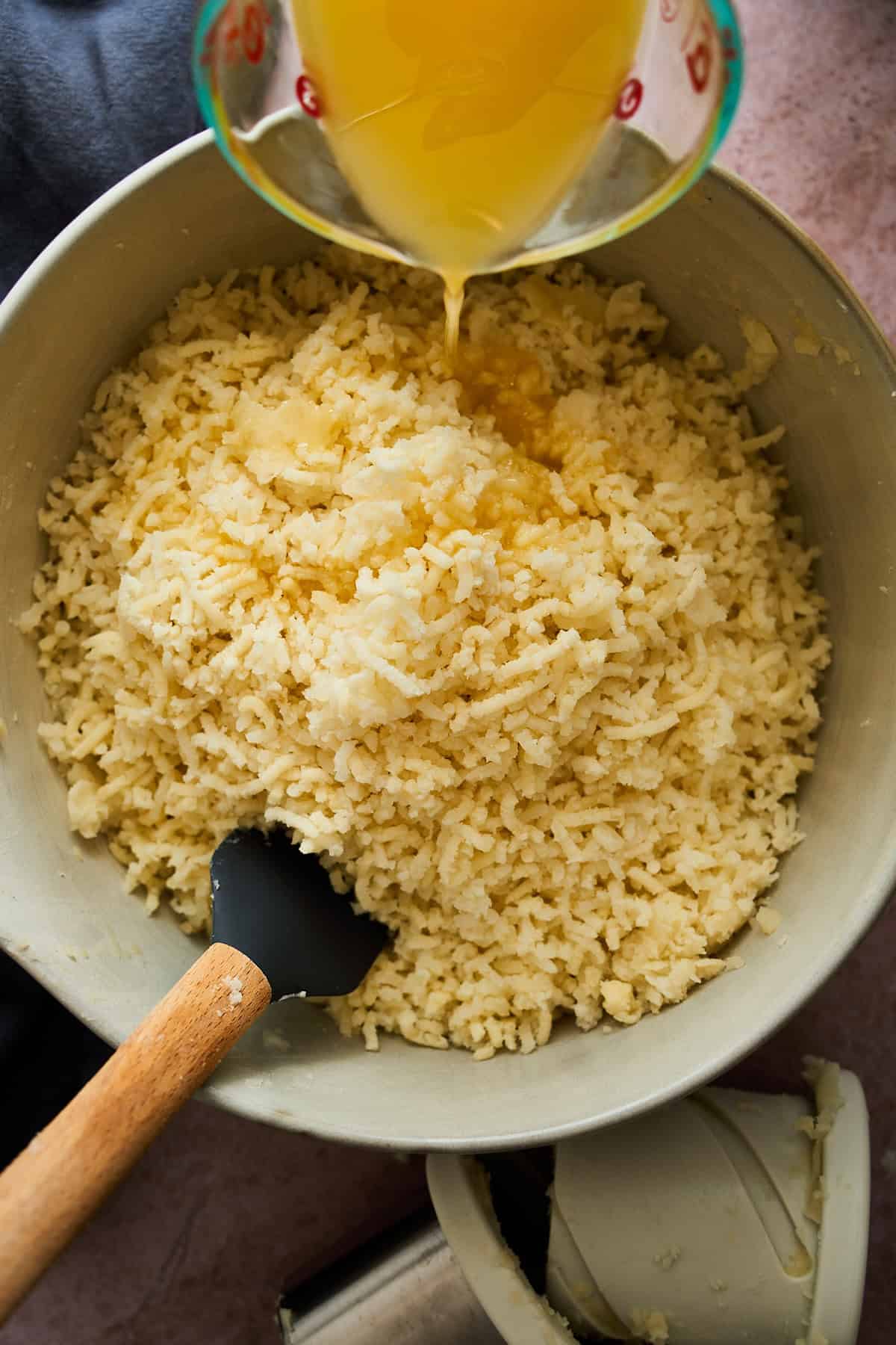 Adding hot butter to riced potatoes.