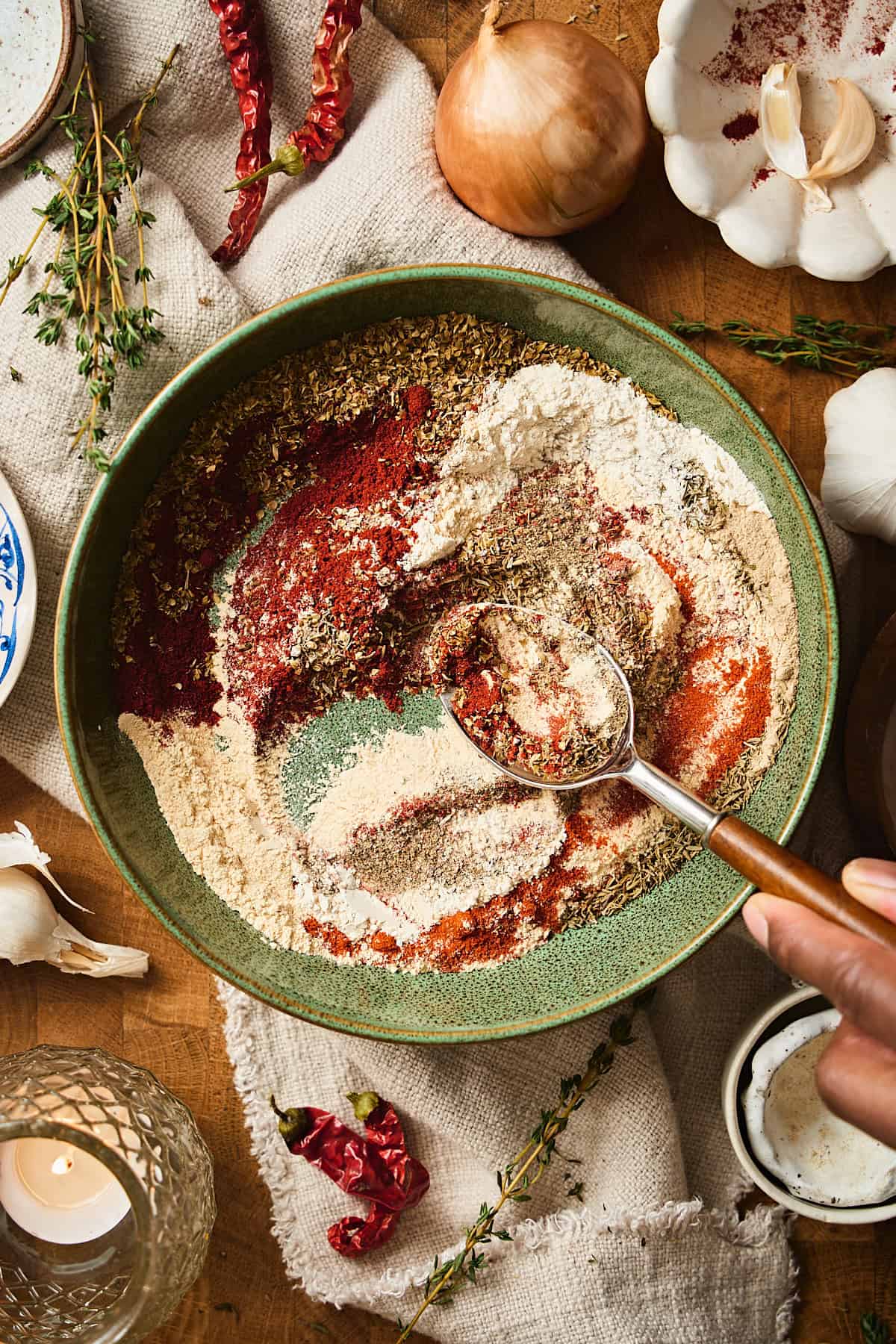 Hand stirring a seasoning mixture in a green bowl with a wooden and silver spoon.