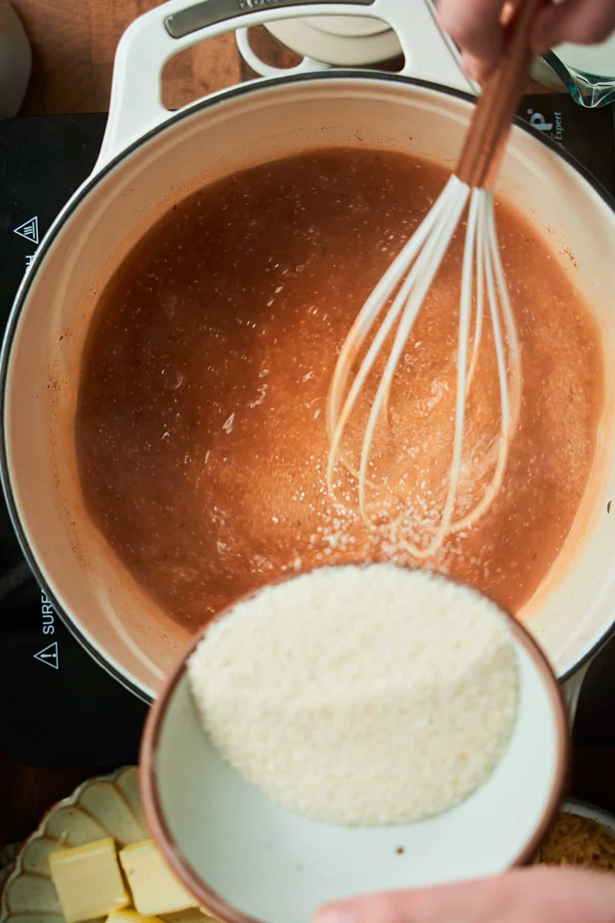 Pouring in white grits in a Dutch oven with stock and whisking in the grits slowly.