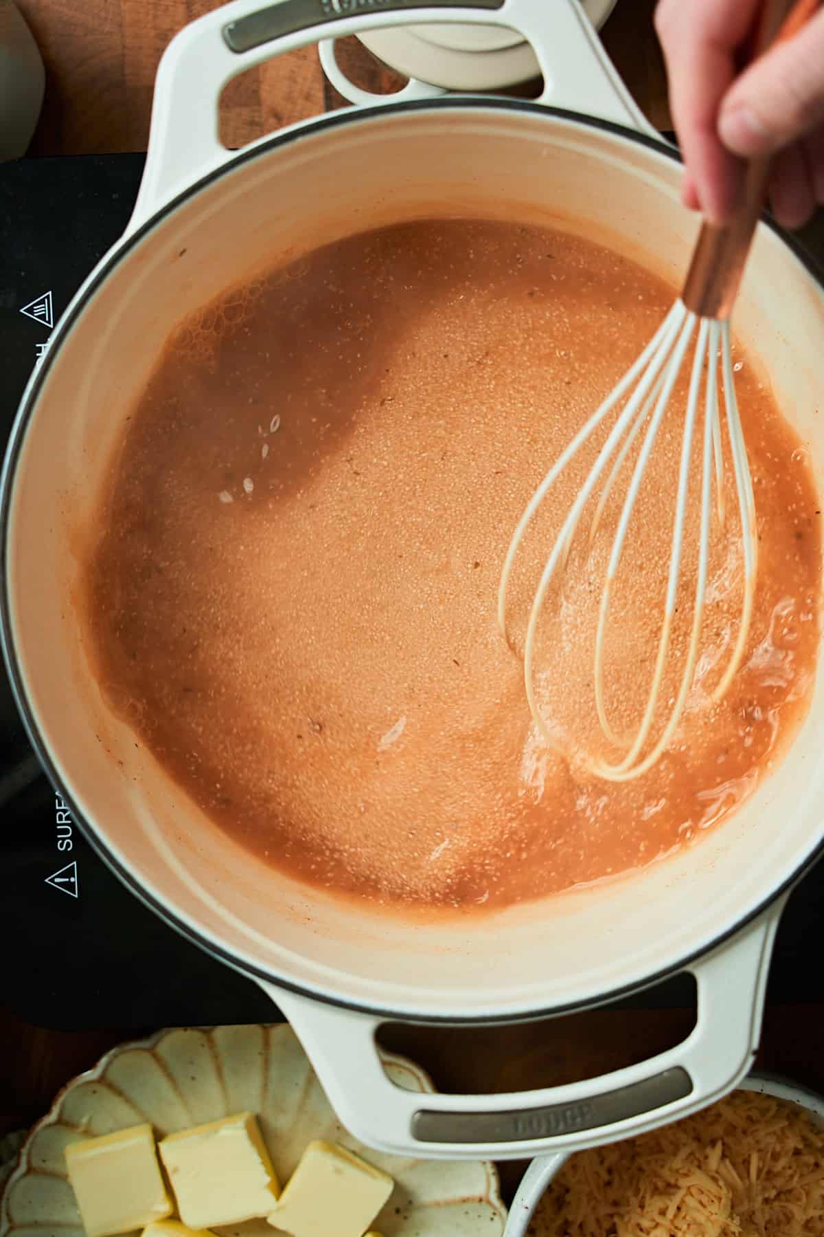 Whisking grits in a flavorful stock while the grits thicken.