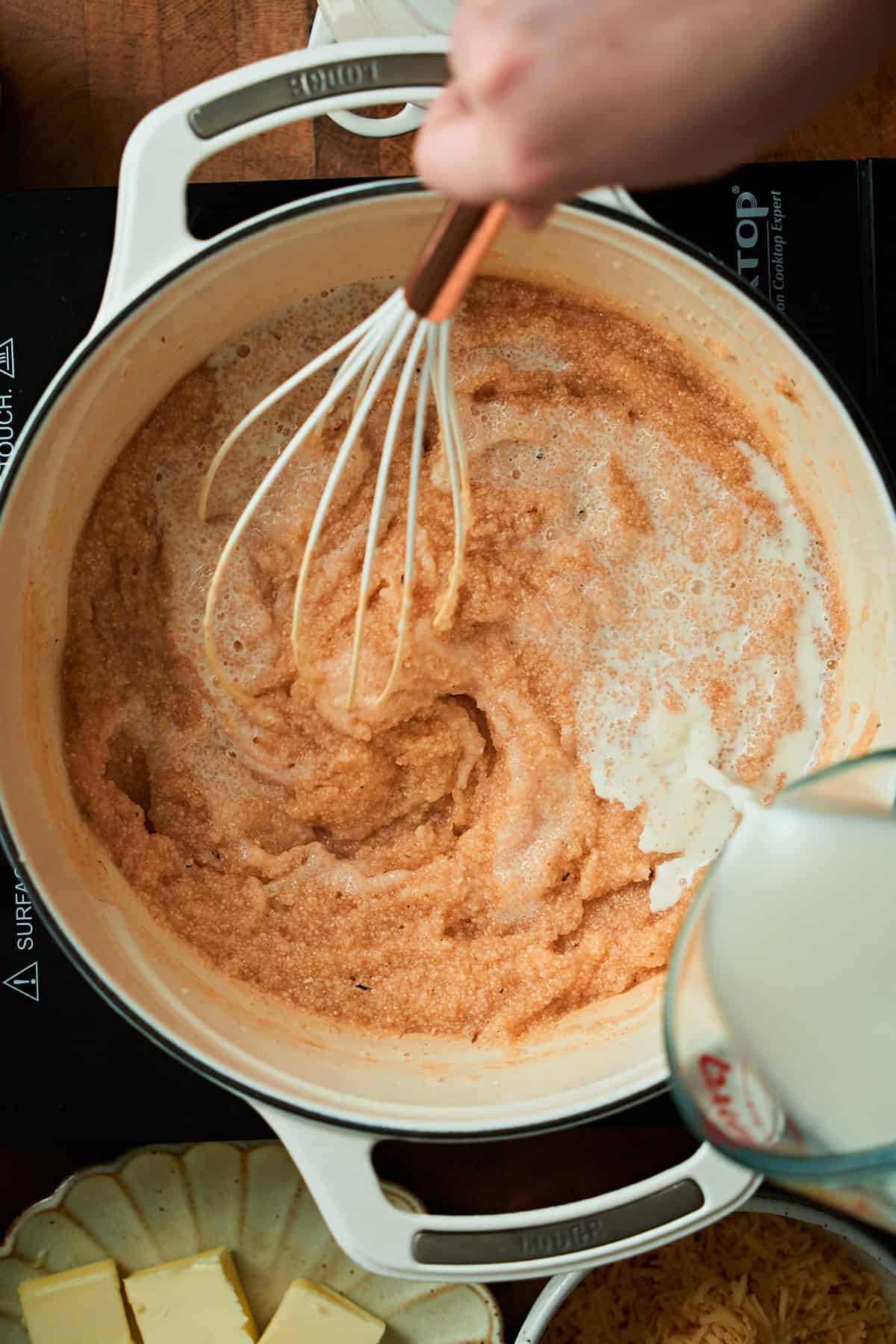 Pouring milk into grits while whisking in a Dutch oven.