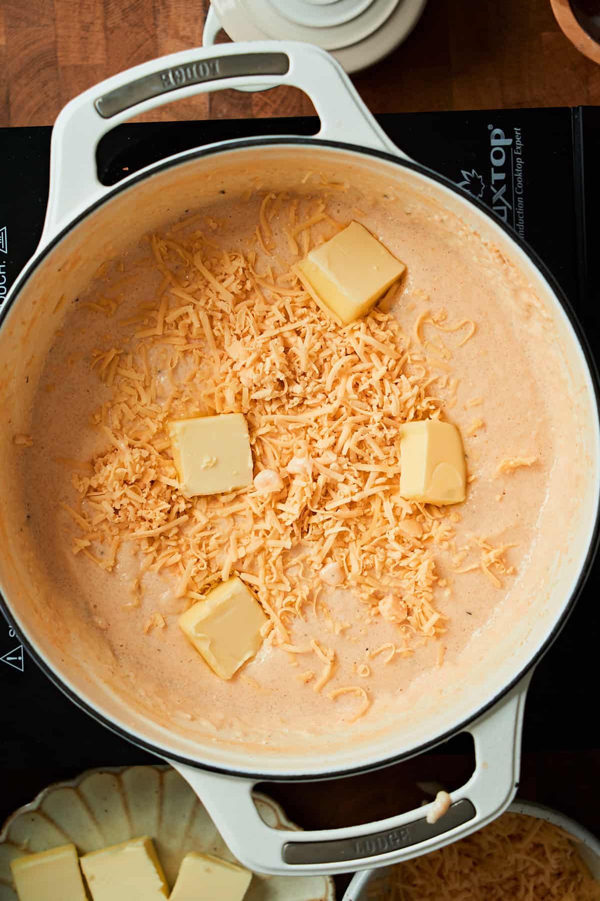Butter and cheese being added to grits in a small Dutch oven.