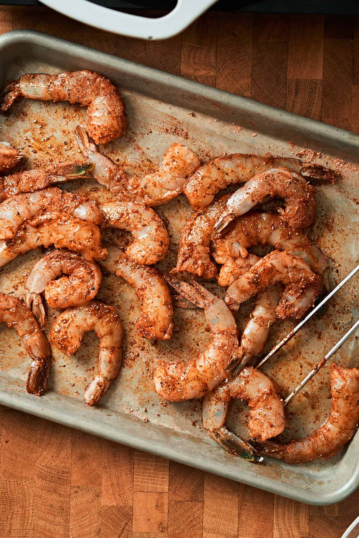 Shrimp seasoned in Cajun seasoning and oil on a baking sheet.