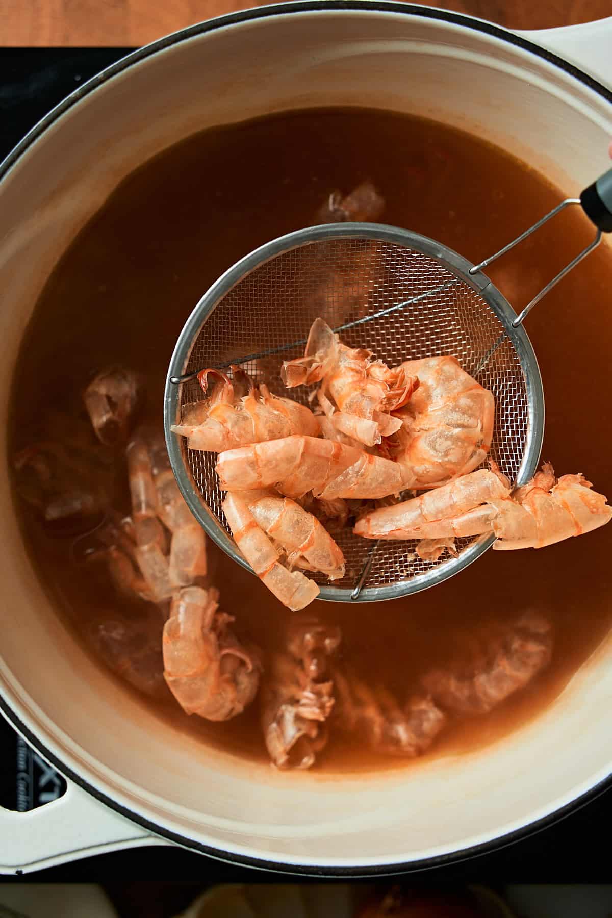 Seafood cooking in broth with a strainer scoop to strain out the shells.
