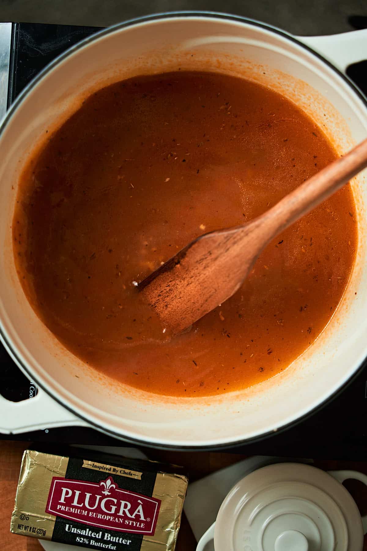 Butter and garlic in a Dutch oven with stock added and a spoon being used to stir.
