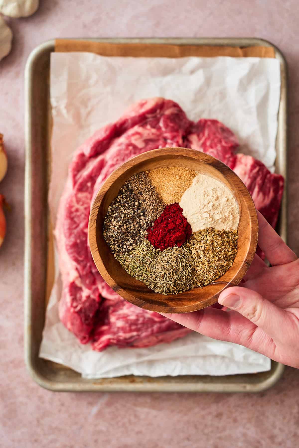 Photo of a hand holding seasonings above a chuck roast.