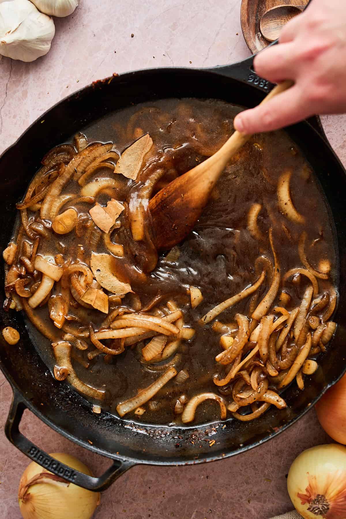 Stirring beef broth and Worcestershire sauce in a skillet with onions.