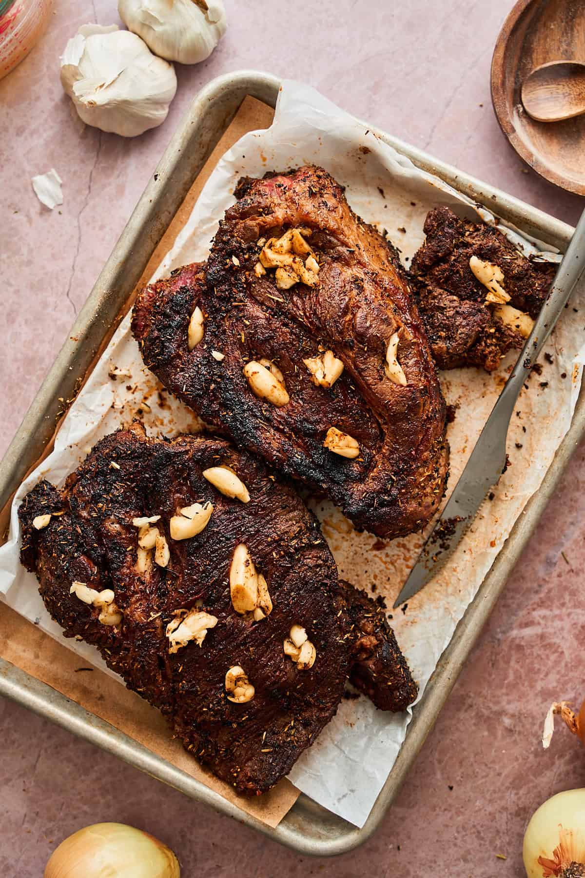 Seared chuck roast on a baking sheet with smashed garlic cloves.