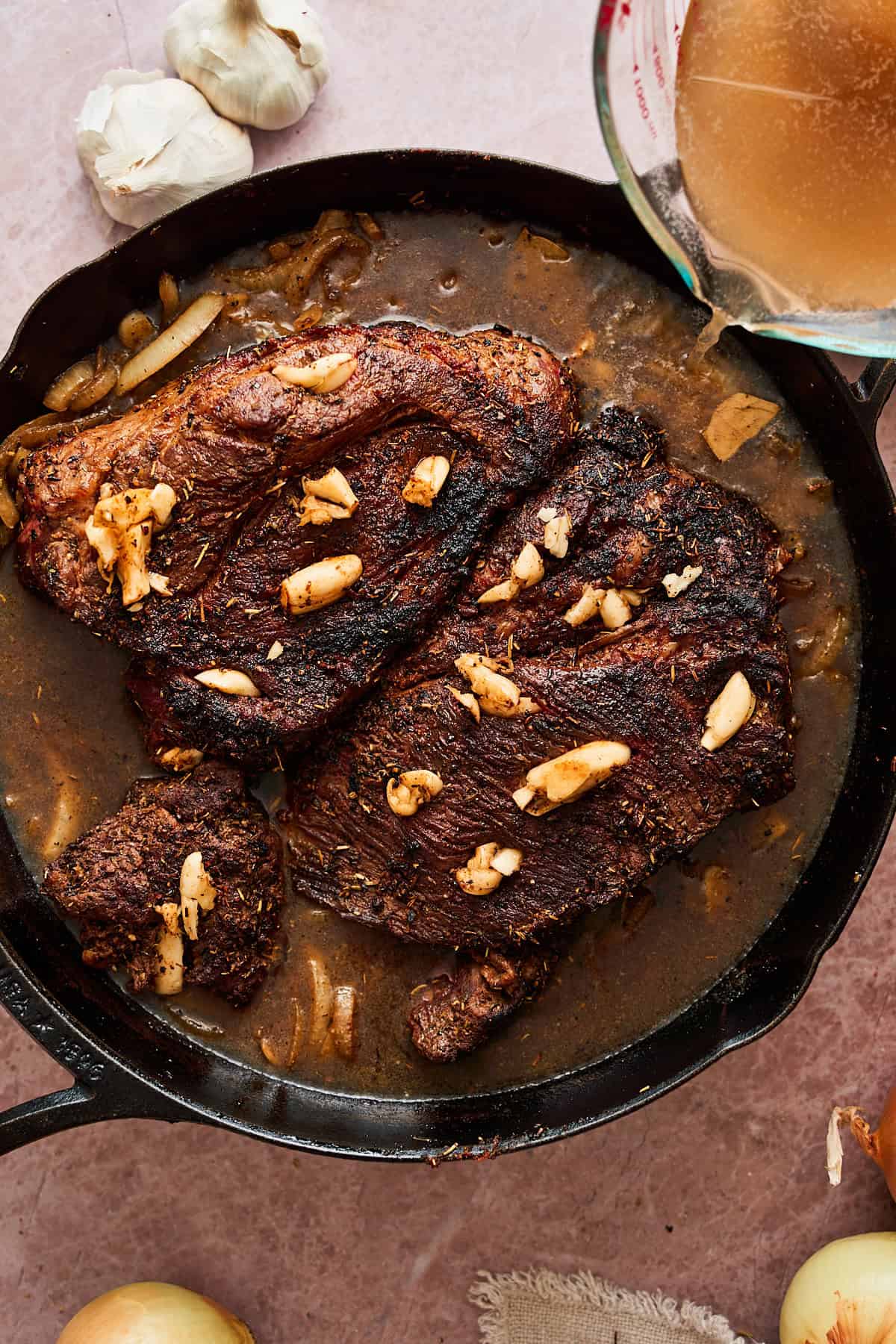 Pouring in beef broth in a skillet with chuck roast stuffed with garlic.