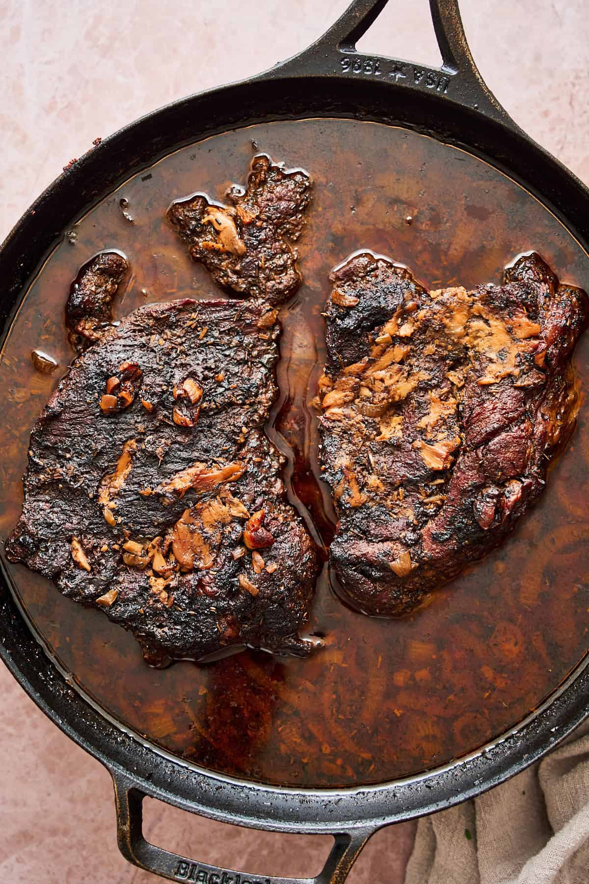 Cooked chuck roast in a cast iron skillet with lots of pan drippings in the pan.