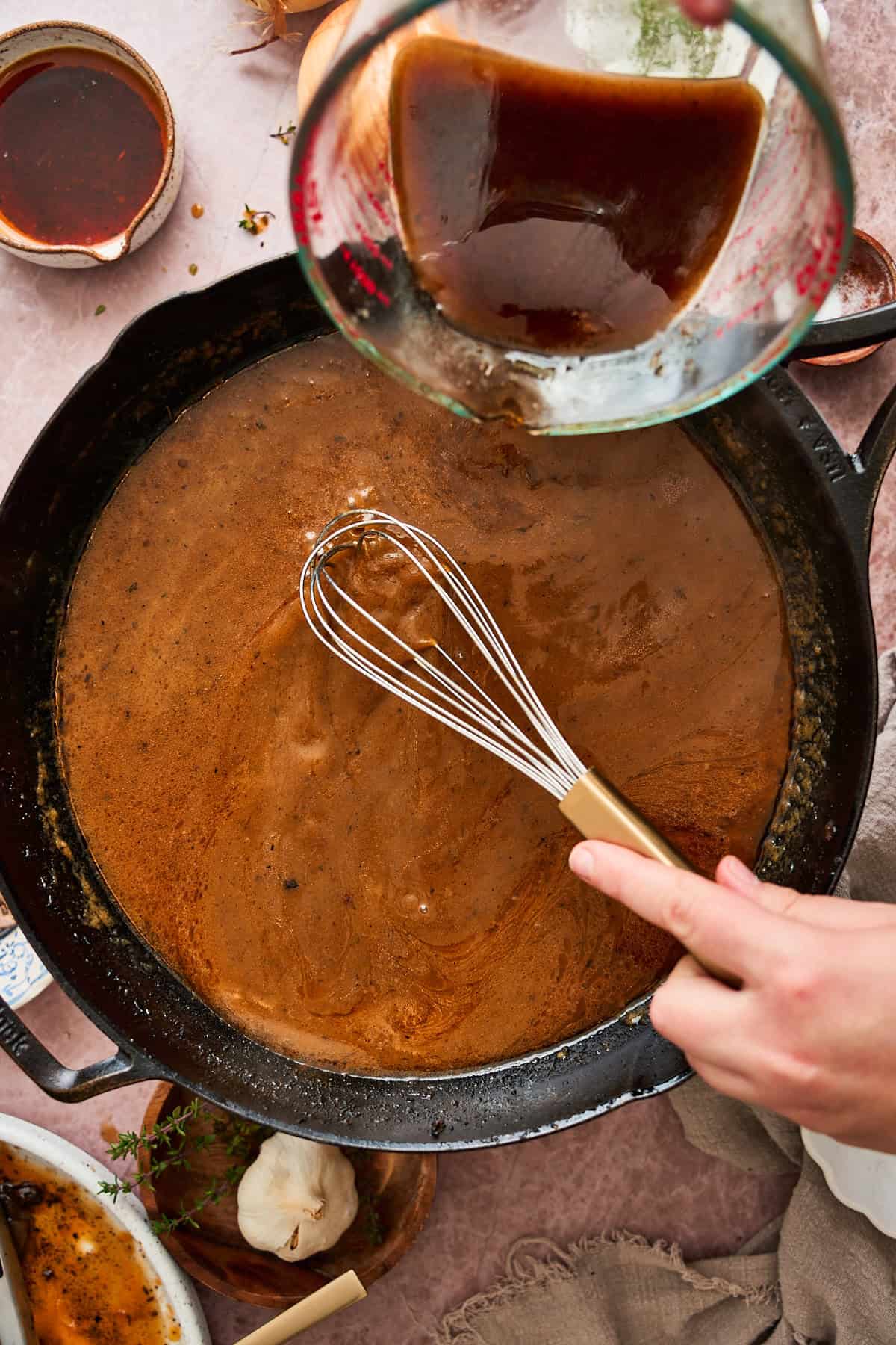 Whisking in beef broth to make gravy in a pan.
